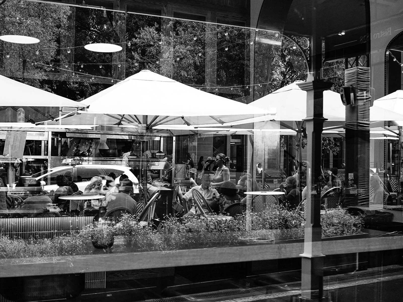 People dining at an outdoor cafe with umbrellas, reflected in a window.