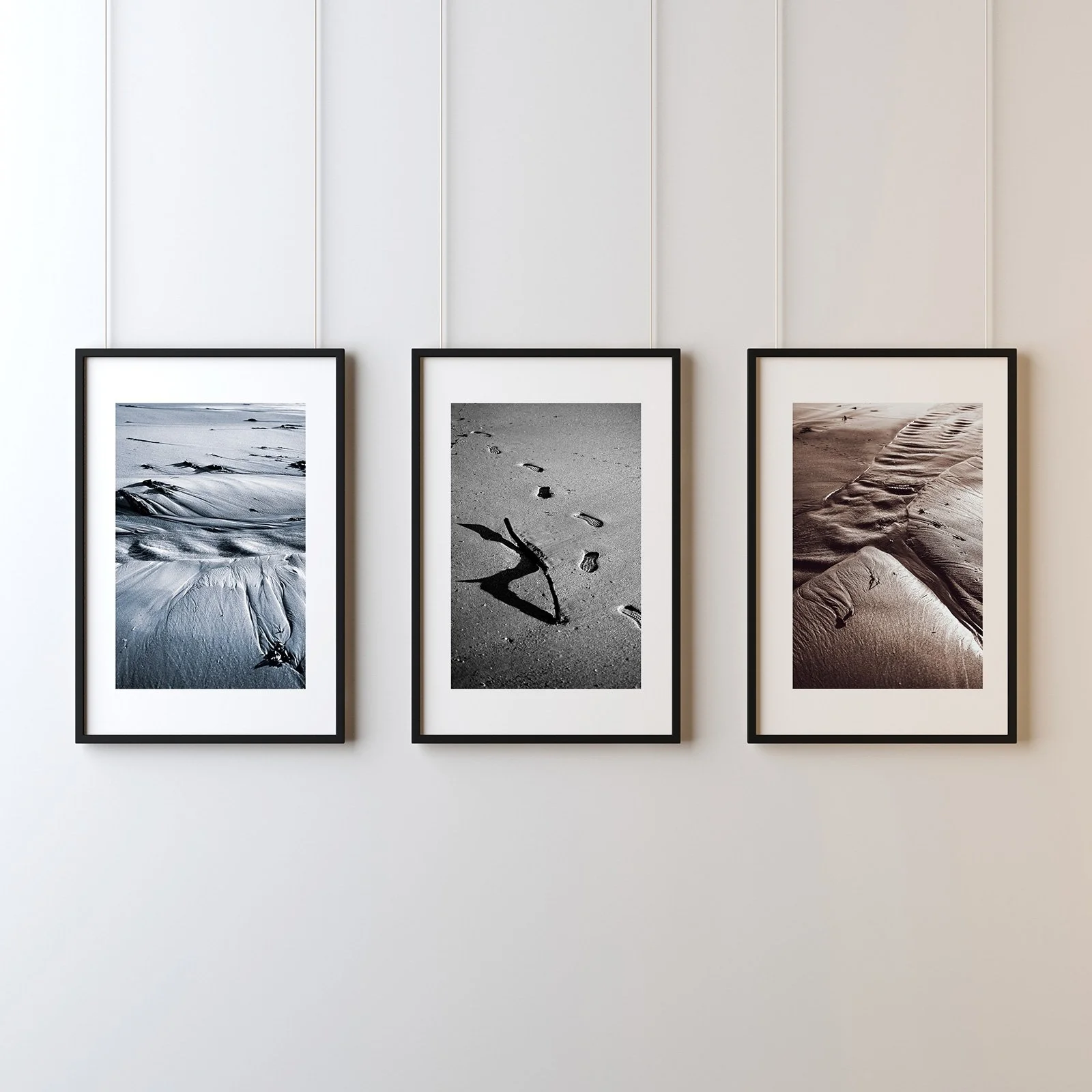 Three framed black and white photographs of beach scenes hanging on a white wall.