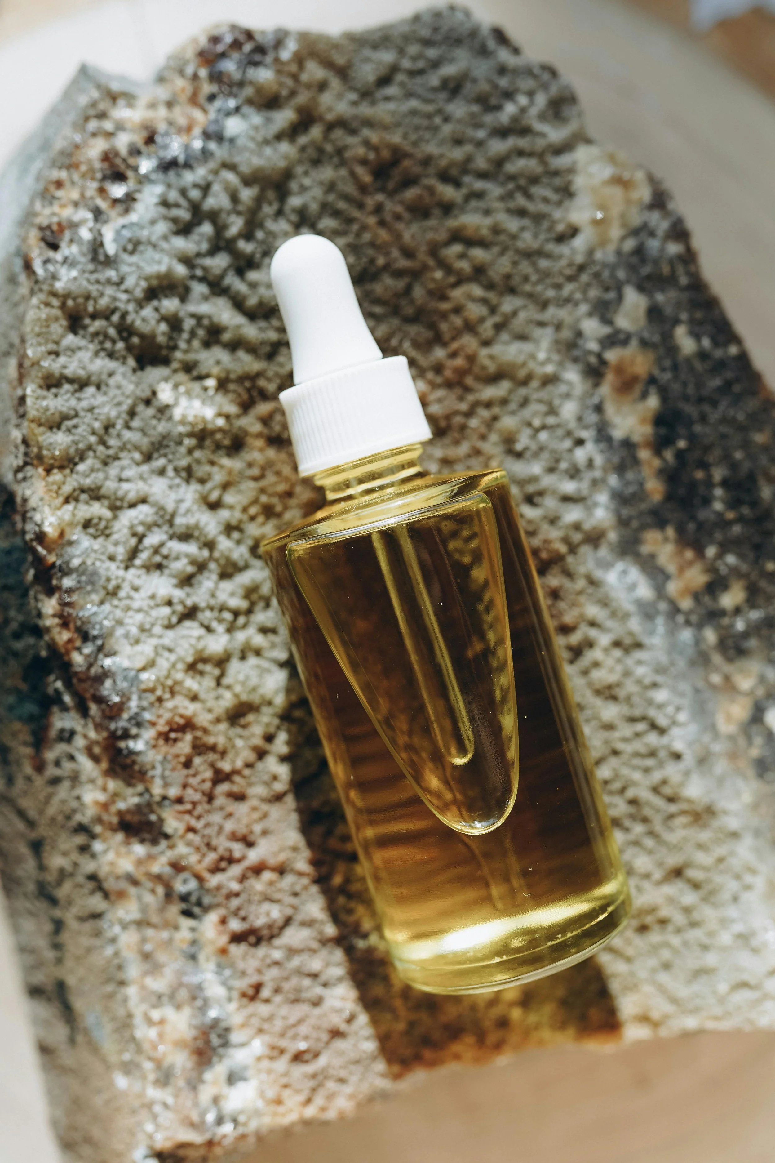 A small glass bottle of golden essential oil placed on a rough, textured rock.