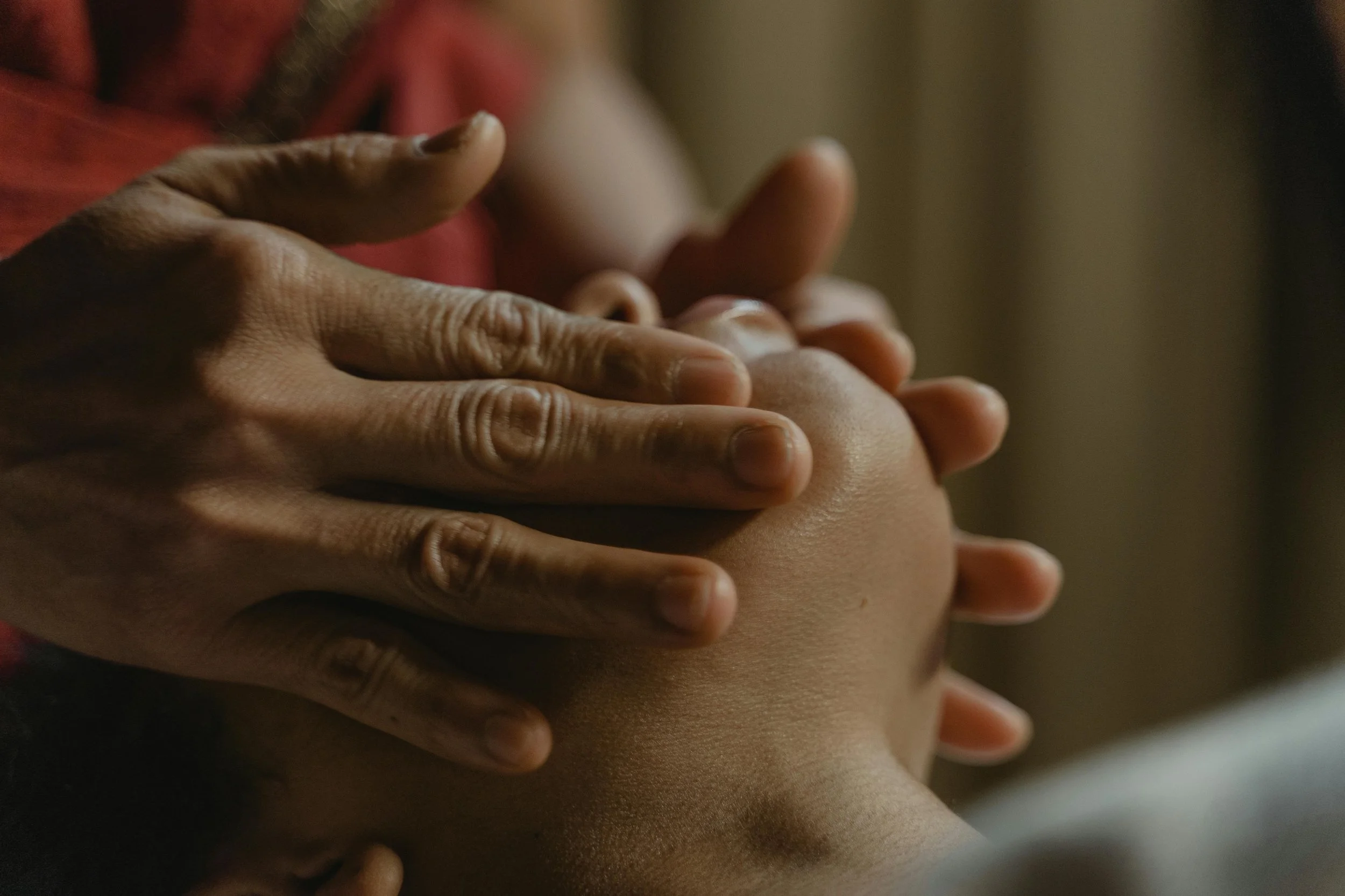 Close-up of hands gently touching and holding a child's head, with a warm, soft focus in the background.