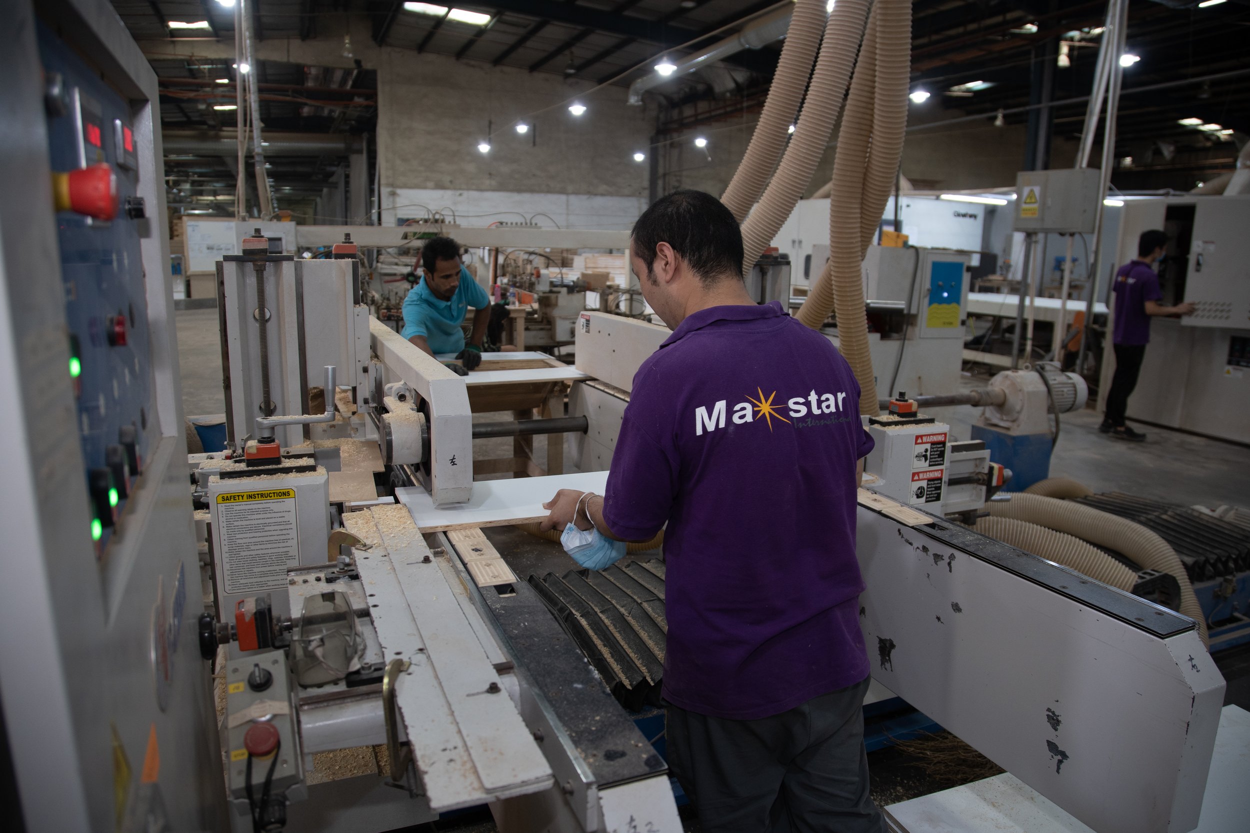 Workers in a manufacturing factory operating machinery and assembling wooden products.