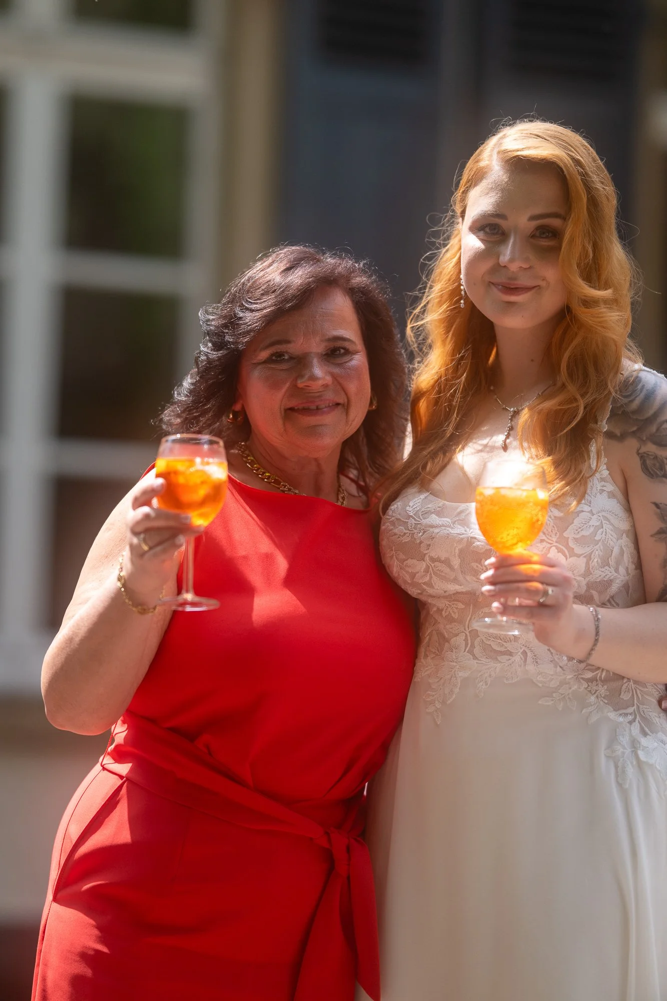 Zwei Frauen bei einer Feier, die in ihren Händen Gläser mit einem orangefarbenen Getränk halten und sich lächelnd ansehen.