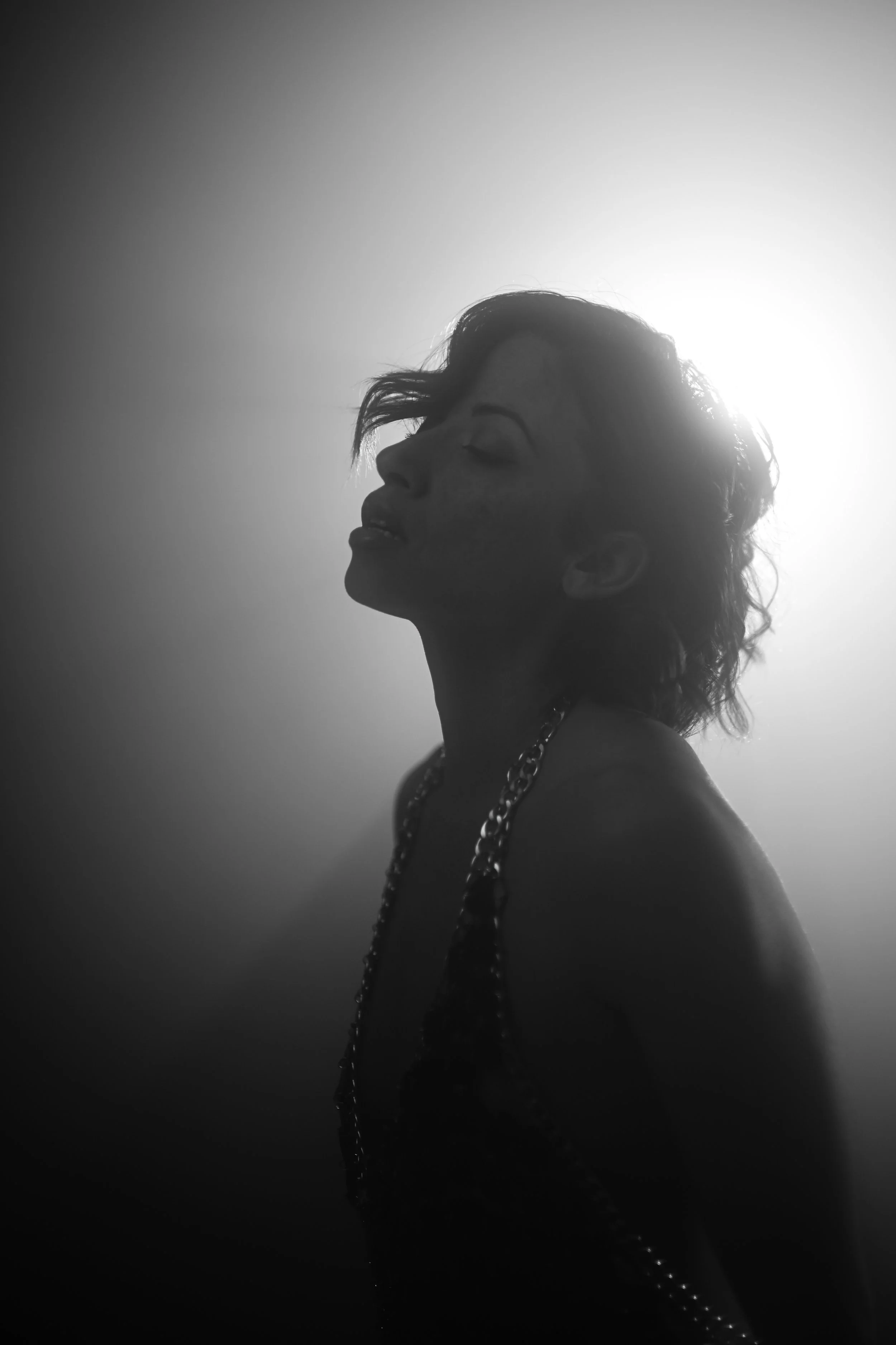 Schwarz-weiß Bild eines Mannes mit geschlossenen Augen, der leicht nach oben schaut, vor hellem Hintergrund, trägt eine Kette.