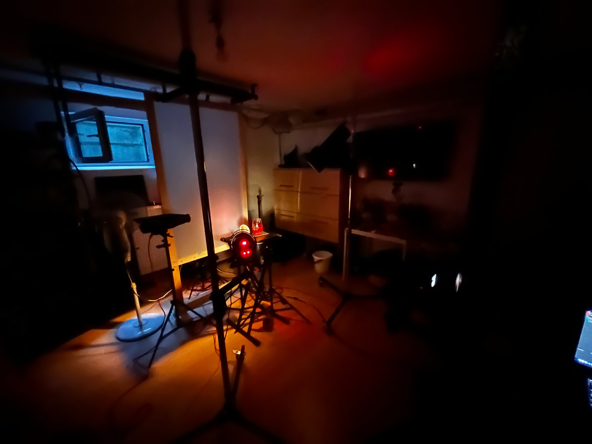 Dunkler Raum mit Musikequipment, einem geöffneten Fenster, einem Fernseher und verschiedenen Gegenständen unter schwachem Licht.