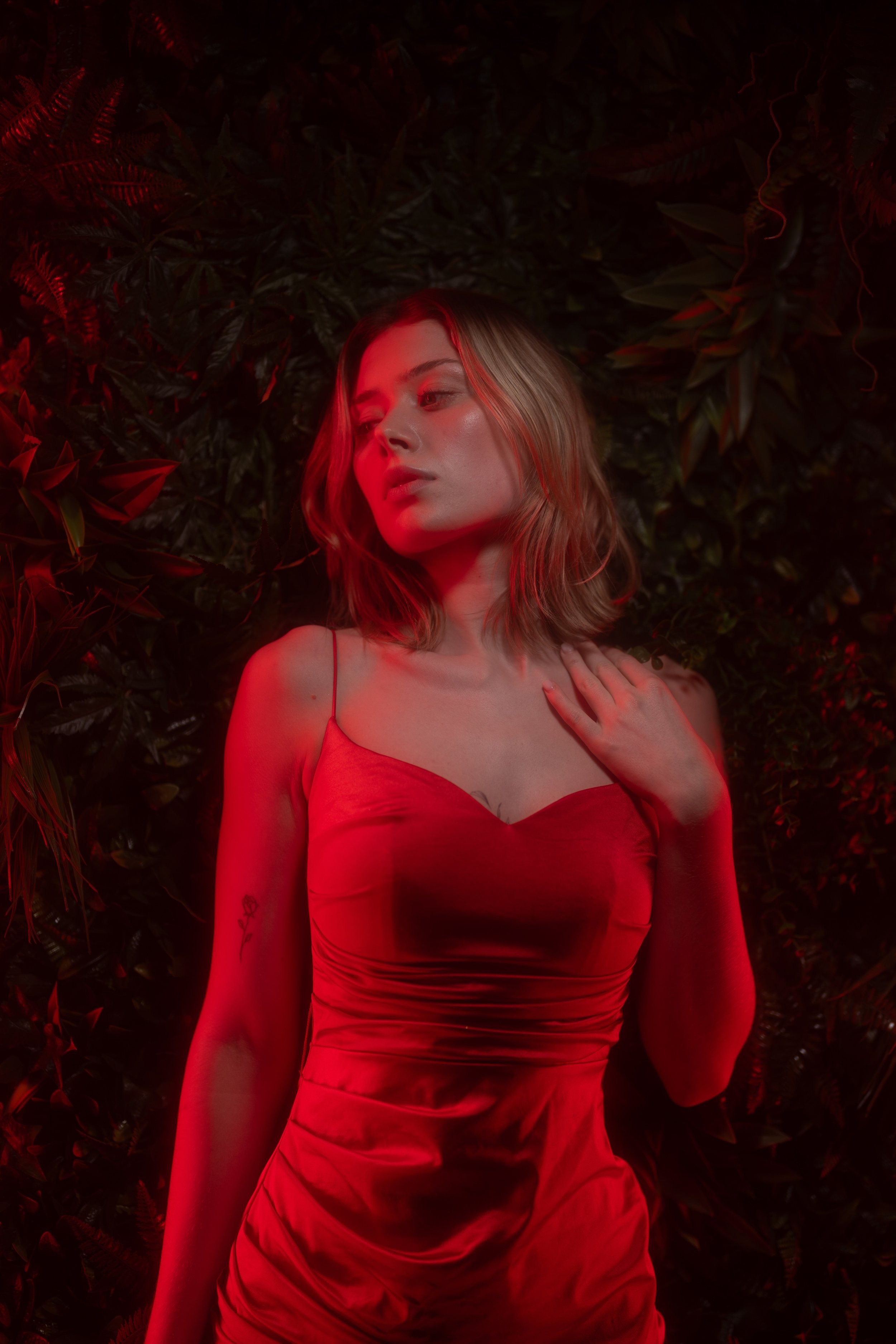 Junge Frau in rotem Kleid vor dunklem, grünen Blattgewächs, rot beleuchtet