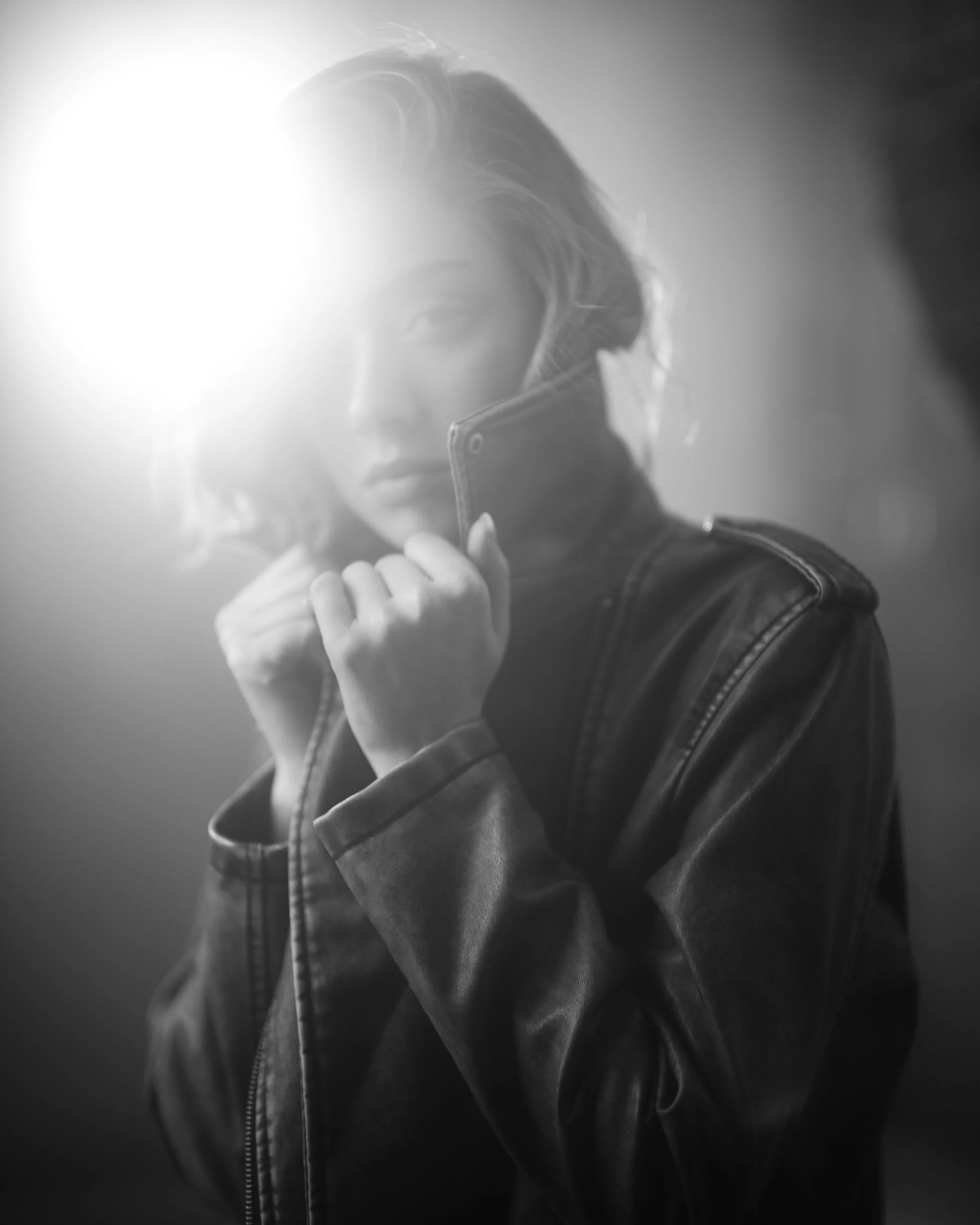 Schwarz-Weiß-Foto eines jungen Mannes, der eine Jacke trägt und ein Handy in der Hand hält, während er in einen Spiegel schaut.