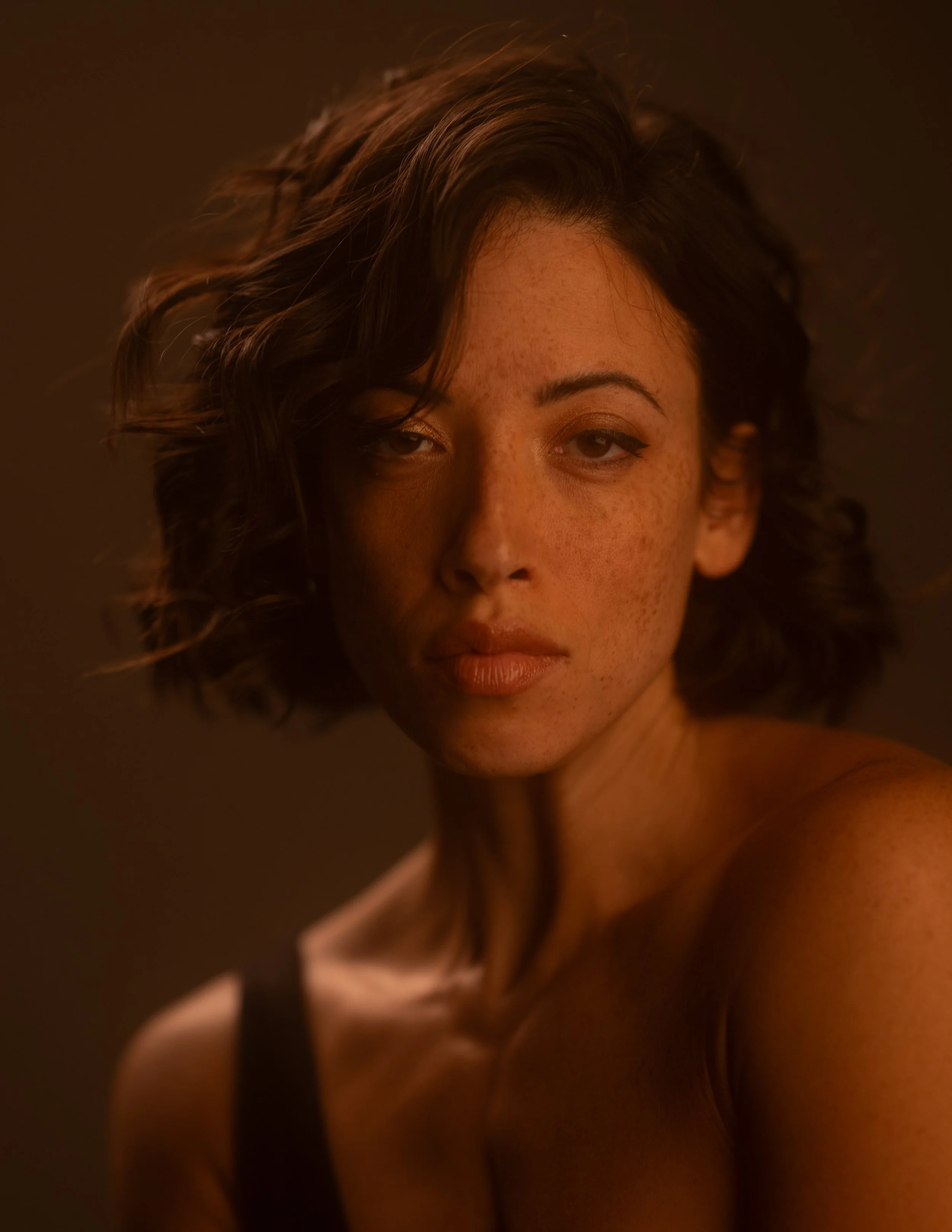 Nahaufnahme eines lächelnden Menschen mit lockigem Haar und Sommersprossen, halb im Schatten, warmes Licht