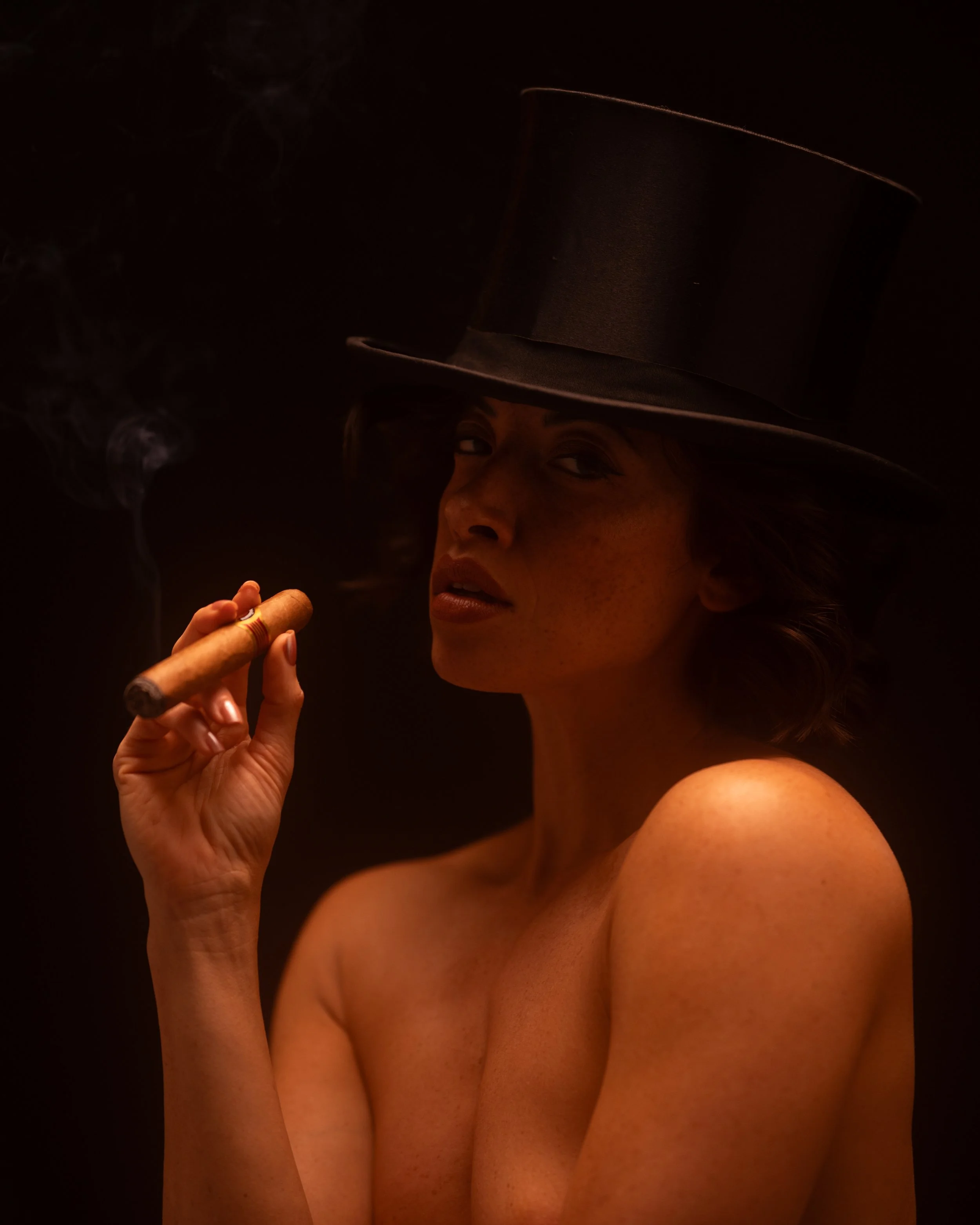 Frau mit nacktem Oberkörper trägt einen schwarzen Zylinderhut und raucht eine Zigarre.