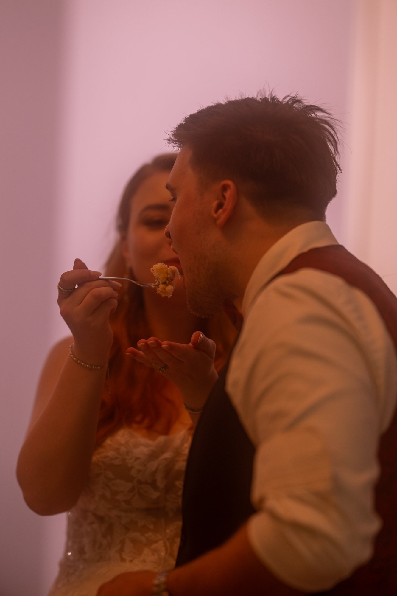 Ein Mann und eine Frau beim Essen auf einer Party, die Frau füttert den Mann mit einem Löffel.