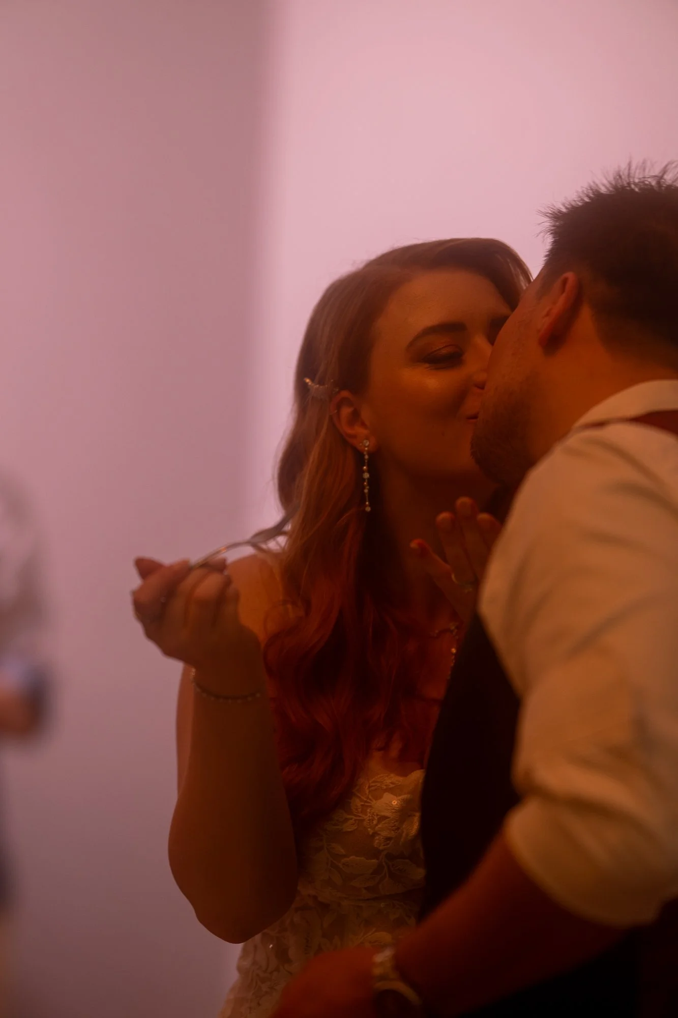 Ein frisch verheiratetes Paar teilt einen Kuss bei ihrer Hochzeit, im Hintergrund in warmem Licht.