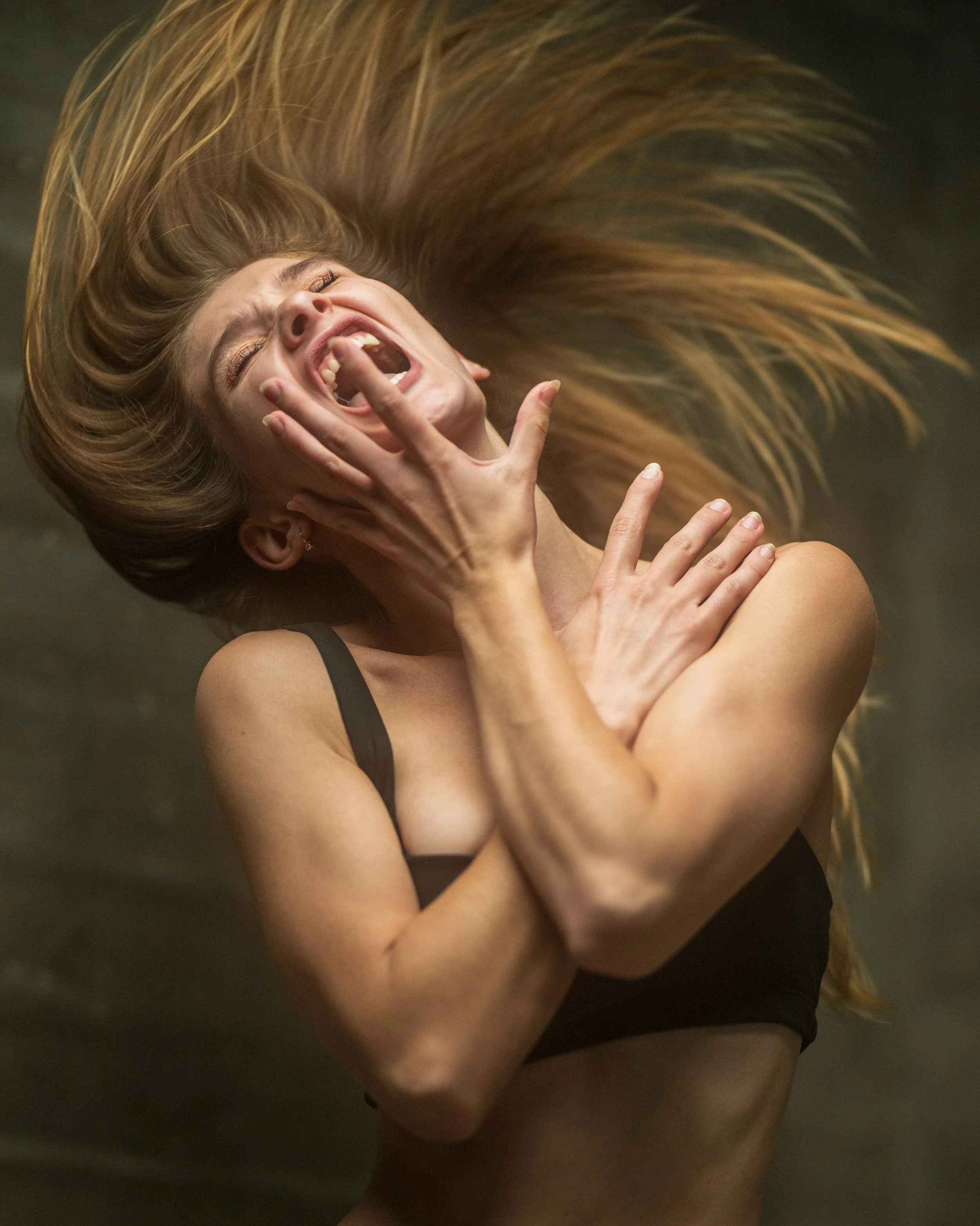 Eine lachende Frau mit langem, hellbraunem Haar, die ihre Augen, Nase und Mund zeigt, während sie die Arme über Kreuz hält.