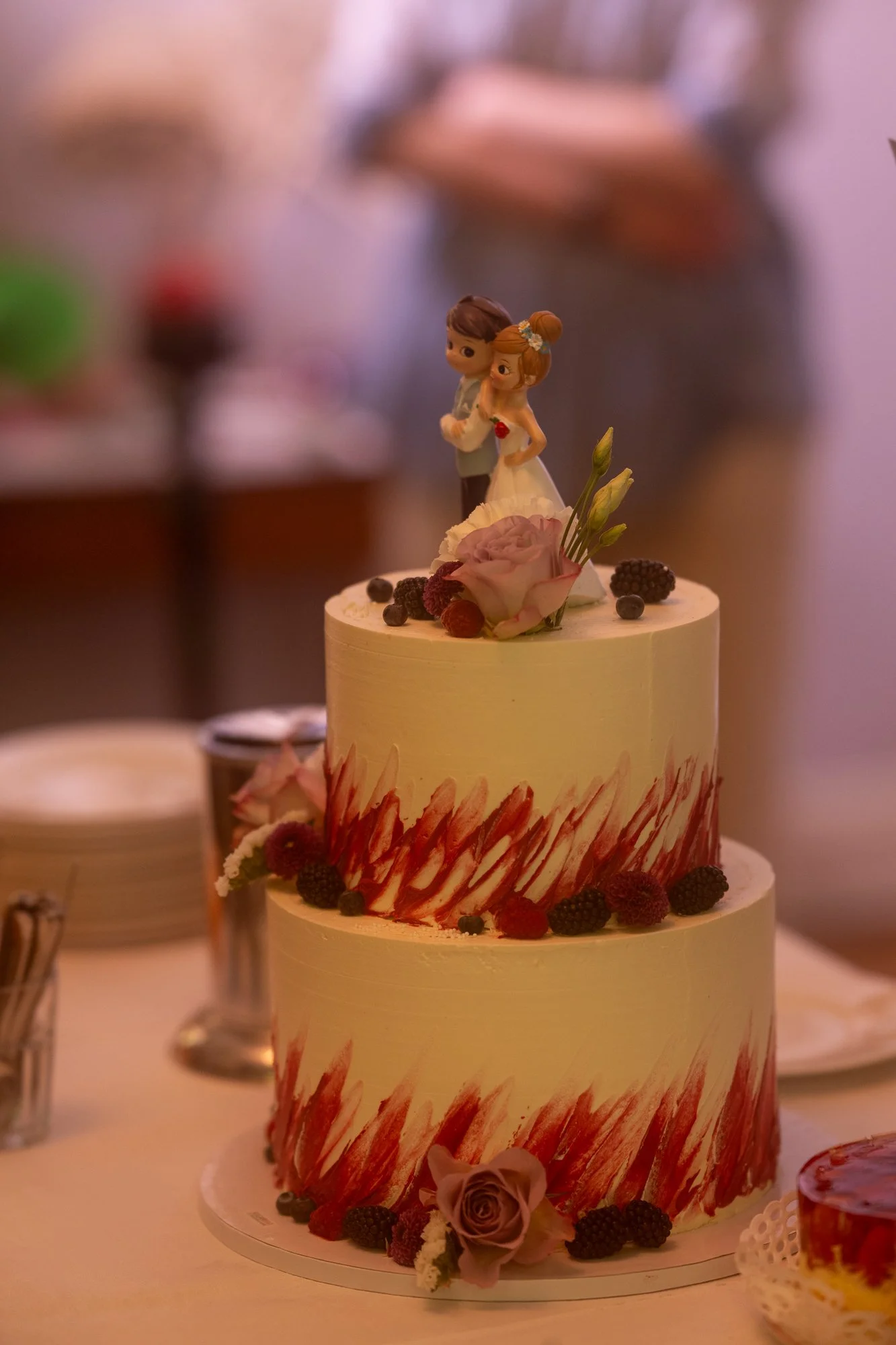 Mehrstöckige Hochzeitstorte mit Figuren eines Brautpaares auf der oberen Ebene, Dekoration mit frischen Blumen und Beeren