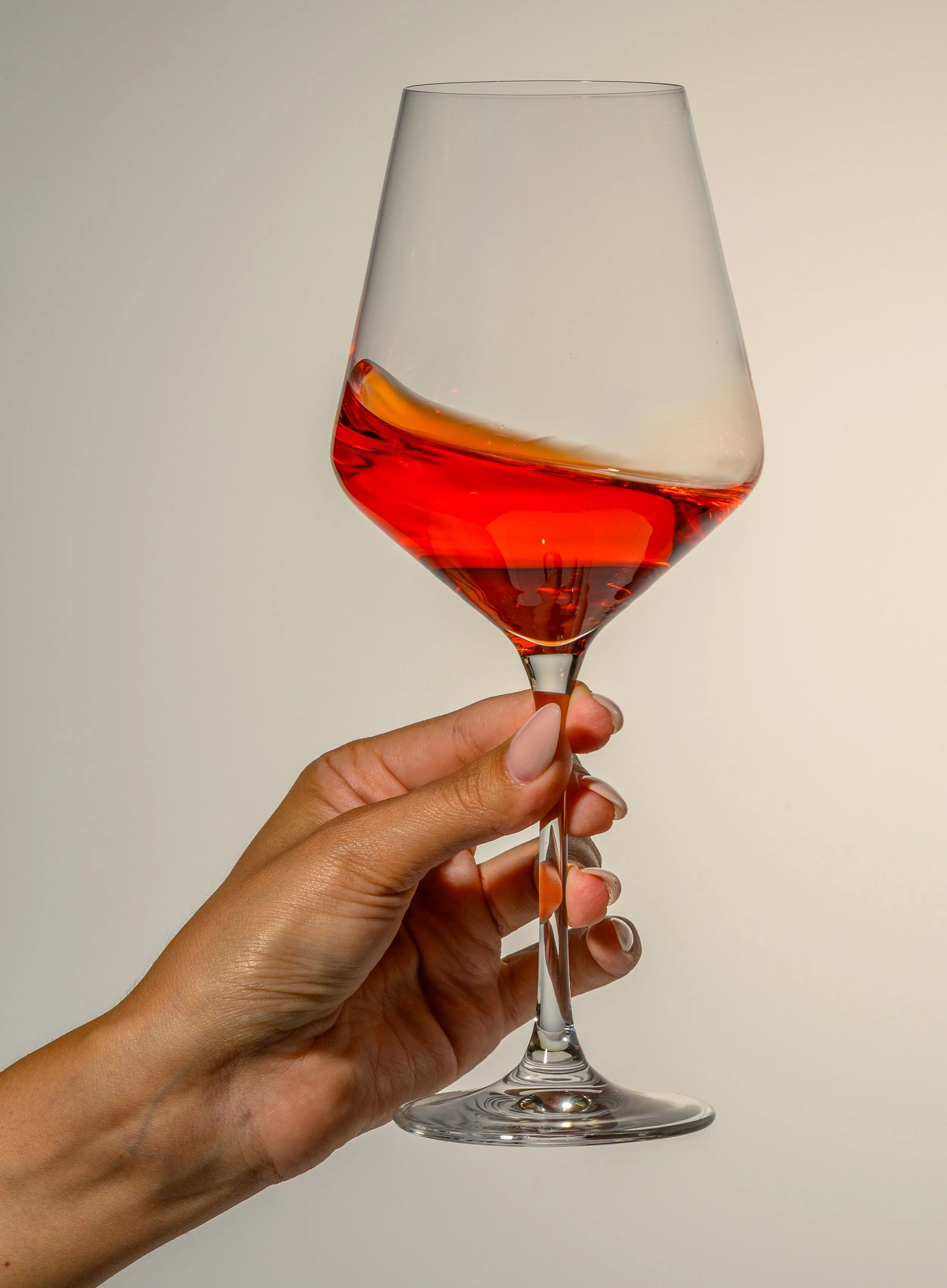 Eine Hand hält ein Weinglas mit rotem Wein vor einem neutralen Hintergrund.