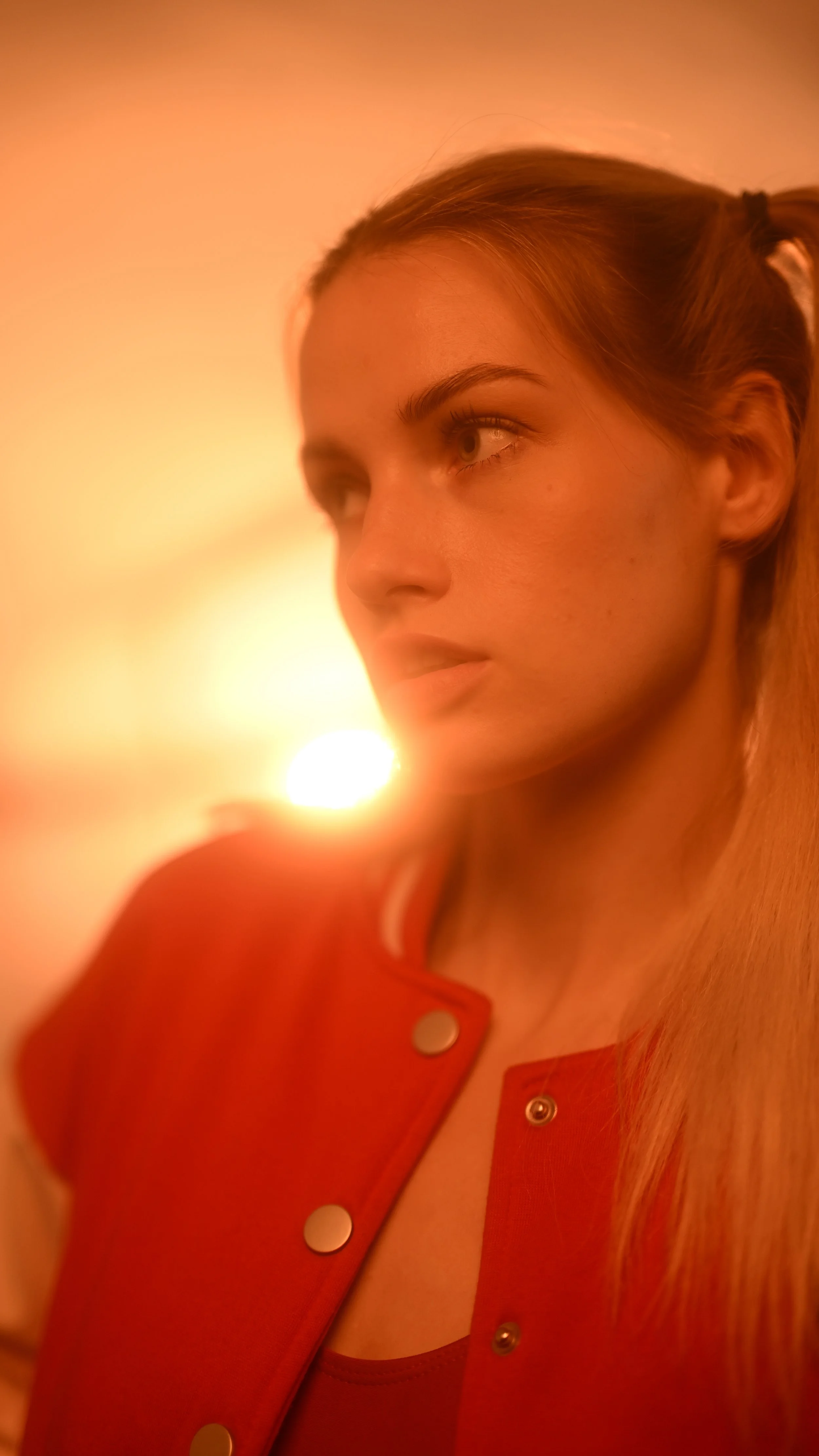 Porträt einer jungen Frau mit rotem Oberteil vor warmem, orangefarbenem Licht