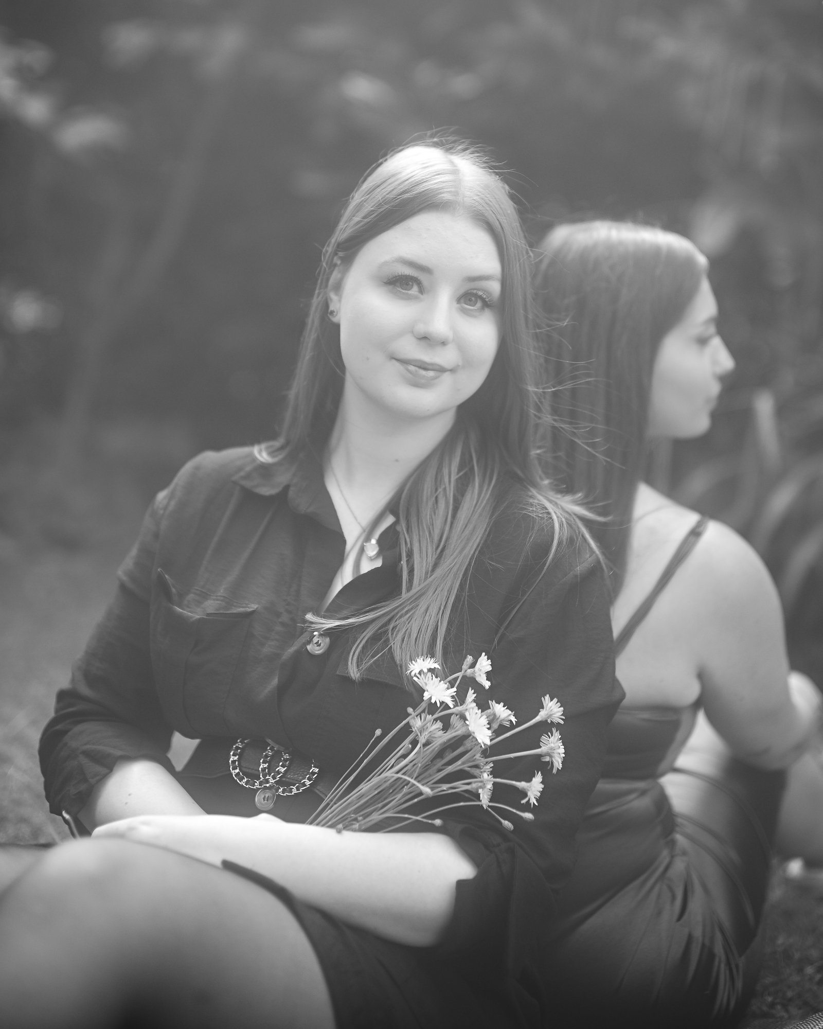 Zwei Frauen sitzen im Freien, die eine Frau hält einen Blumenstrauß.