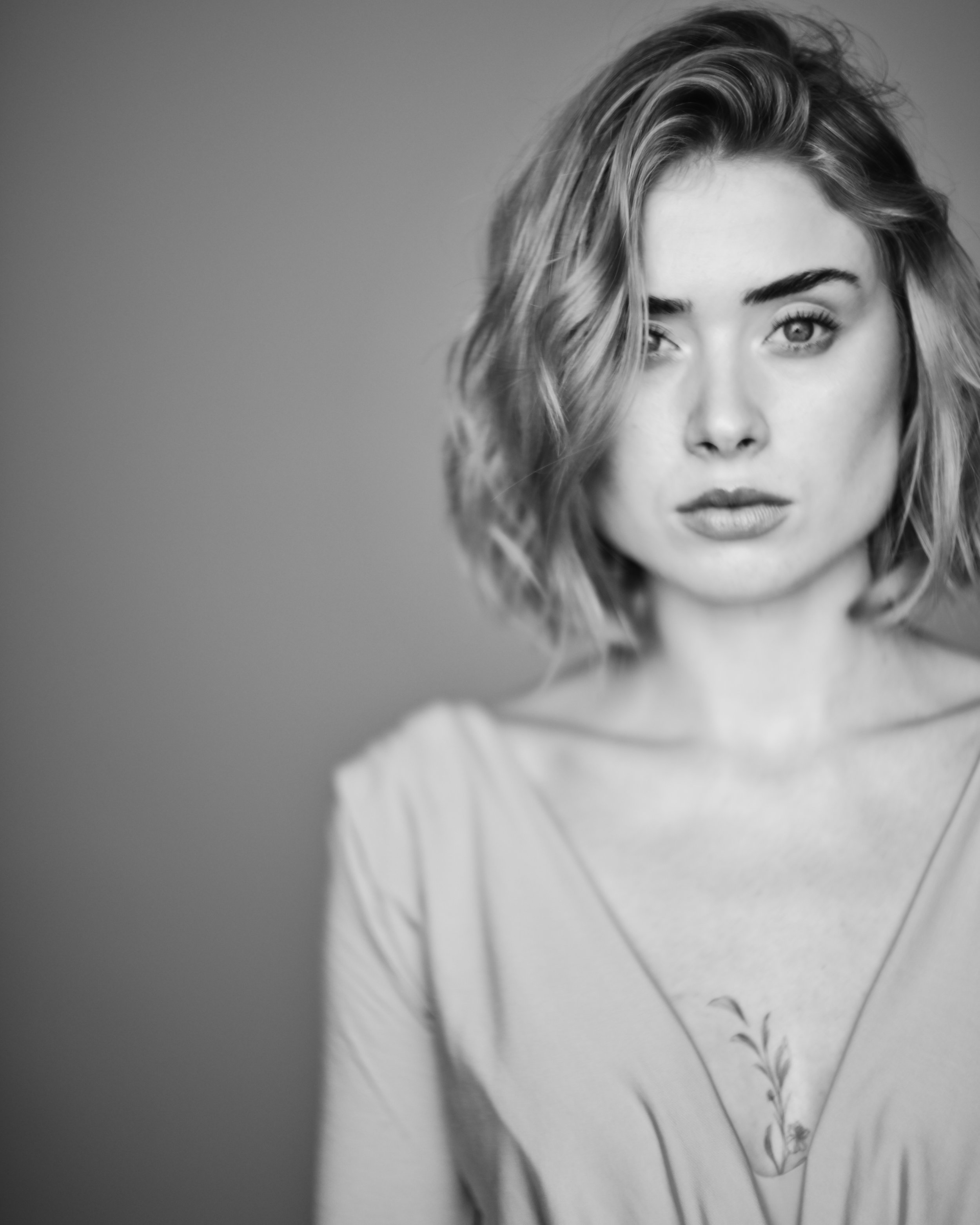 Schwarz-weiß-Fotografie eines jungen Mädchens mit lockigem, mittellangem Haar, Blick in die Kamera, neutraler Hintergrund.