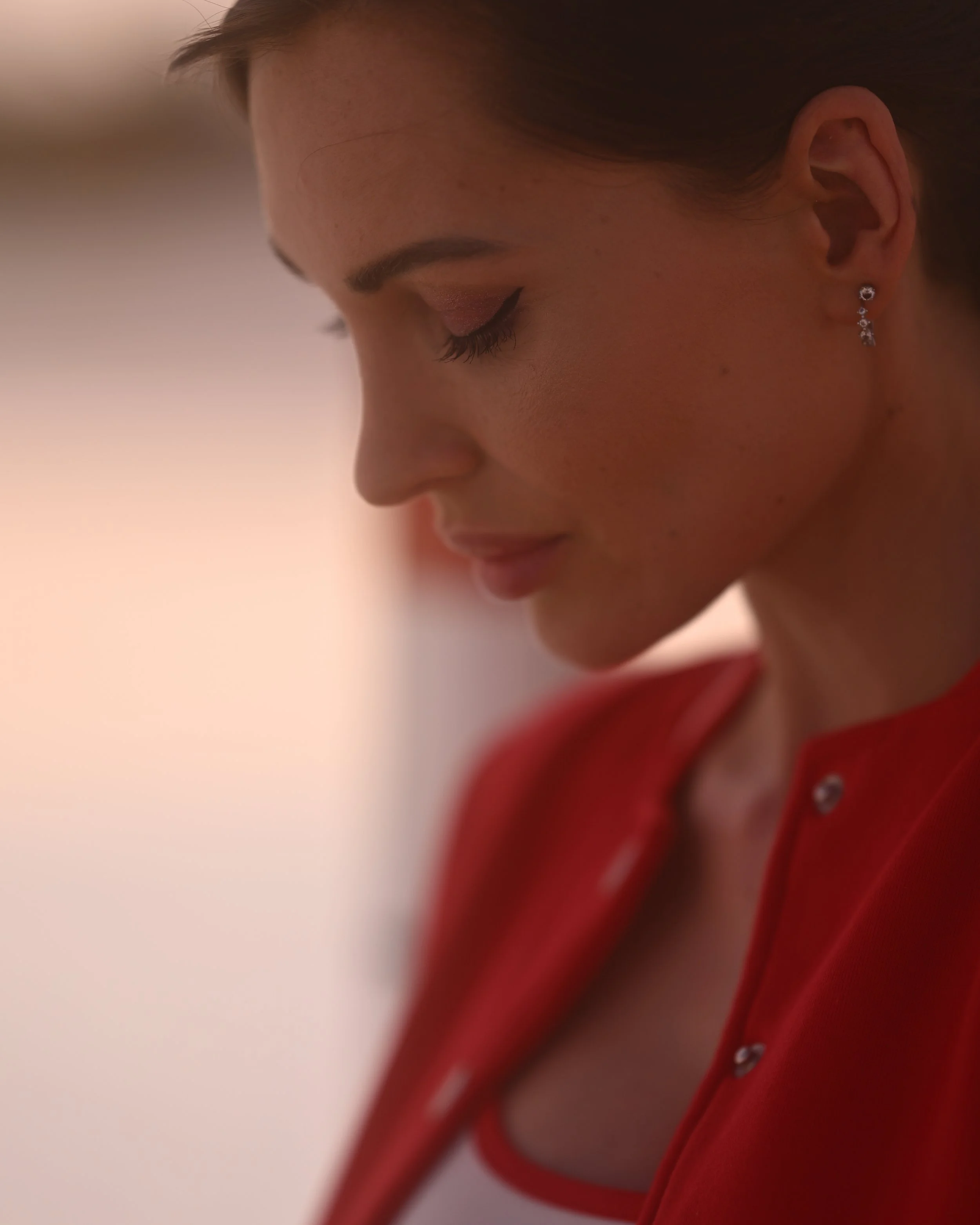 Nahaufnahme eines Gesichts einer jungen Frau mit geschlossenen Augen, auffällig geschminkten Lidern, sowie Ohrringen, trägt einen roten Pullover.