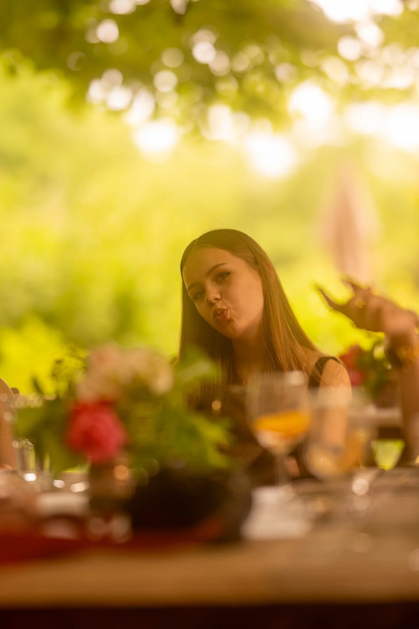 Junge Frau mit langen Haaren, macht ein Kussgesicht, bei einer Feier mit Blumen und Dekoration im Hintergrund.
