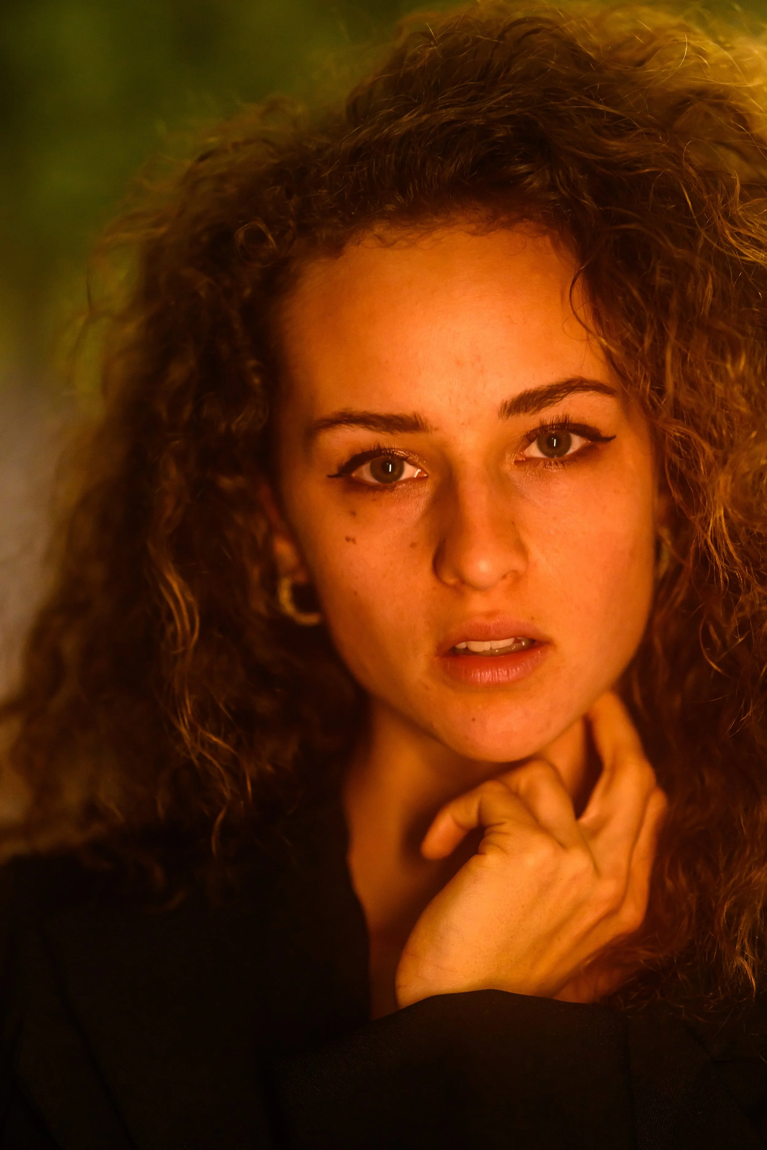 Nahaufnahme eines lächelnden jungen Mädchens mit lockigem braunem Haar, das die Hand an das Kinn legt.