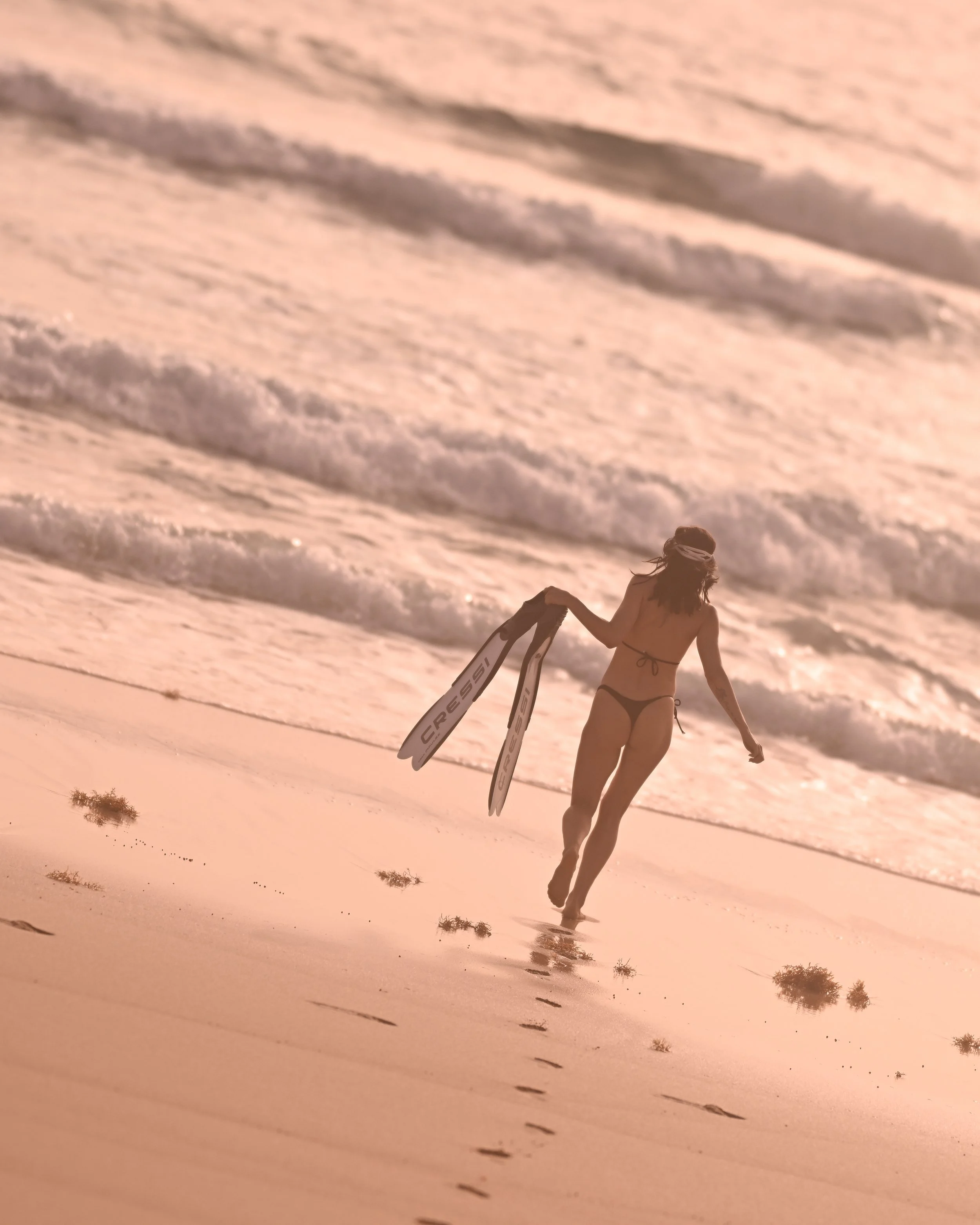 Frau im Bikini mit Skiern läuft am Strand während des Sonnenuntergangs.