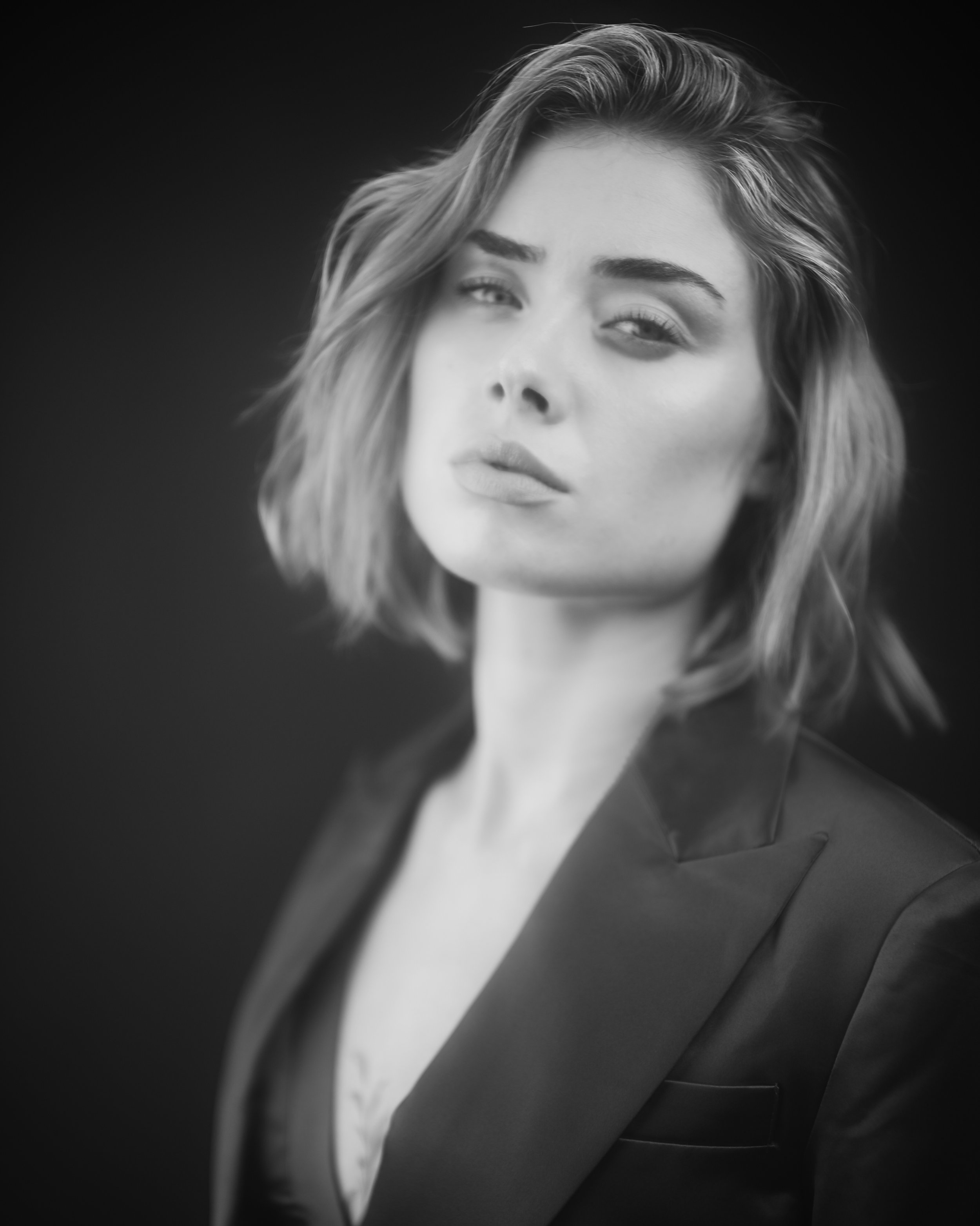 Schwarz-weiß Portrait einer jungen Frau mit geschwungener, mittellanger Frisur, die einen eleganten джеans trägt und direkt in die Kamera schaut.