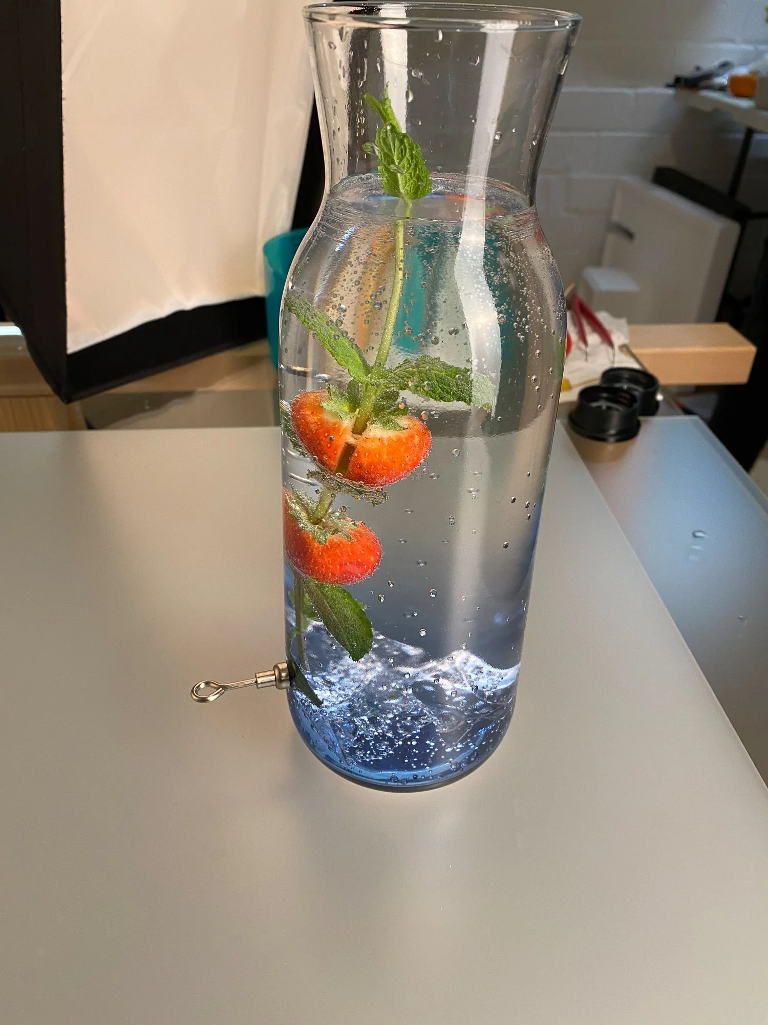 Ein Glas Wasser mit Erdbeeren, Minzblättern und Kohlensäure, das an einem Wasserhahn befestigt ist.