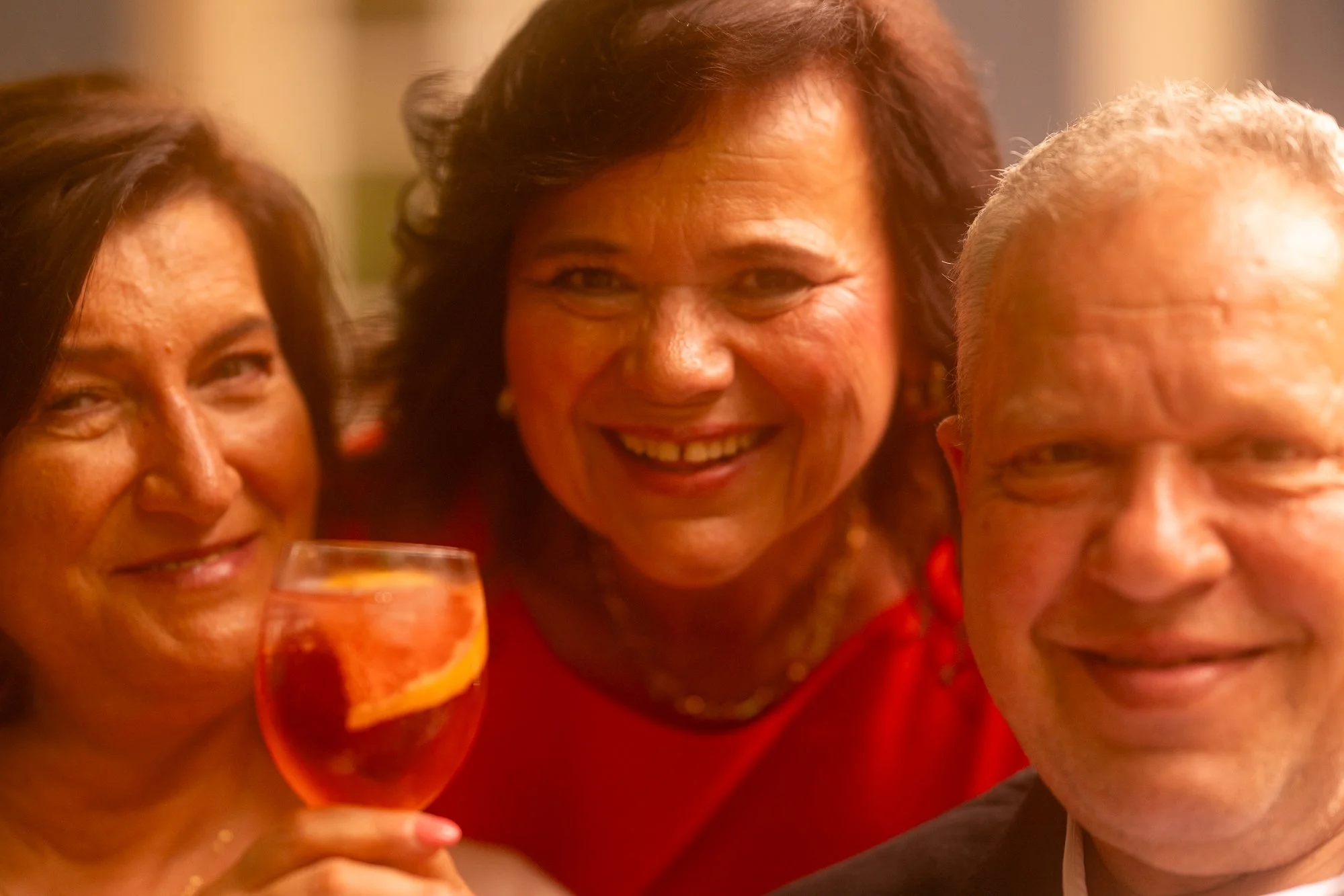Fröhliche Menschen bei einer Feier, einer hält ein Glas mit orangefarbenem Getränk, alle lächeln und haben Spaß.