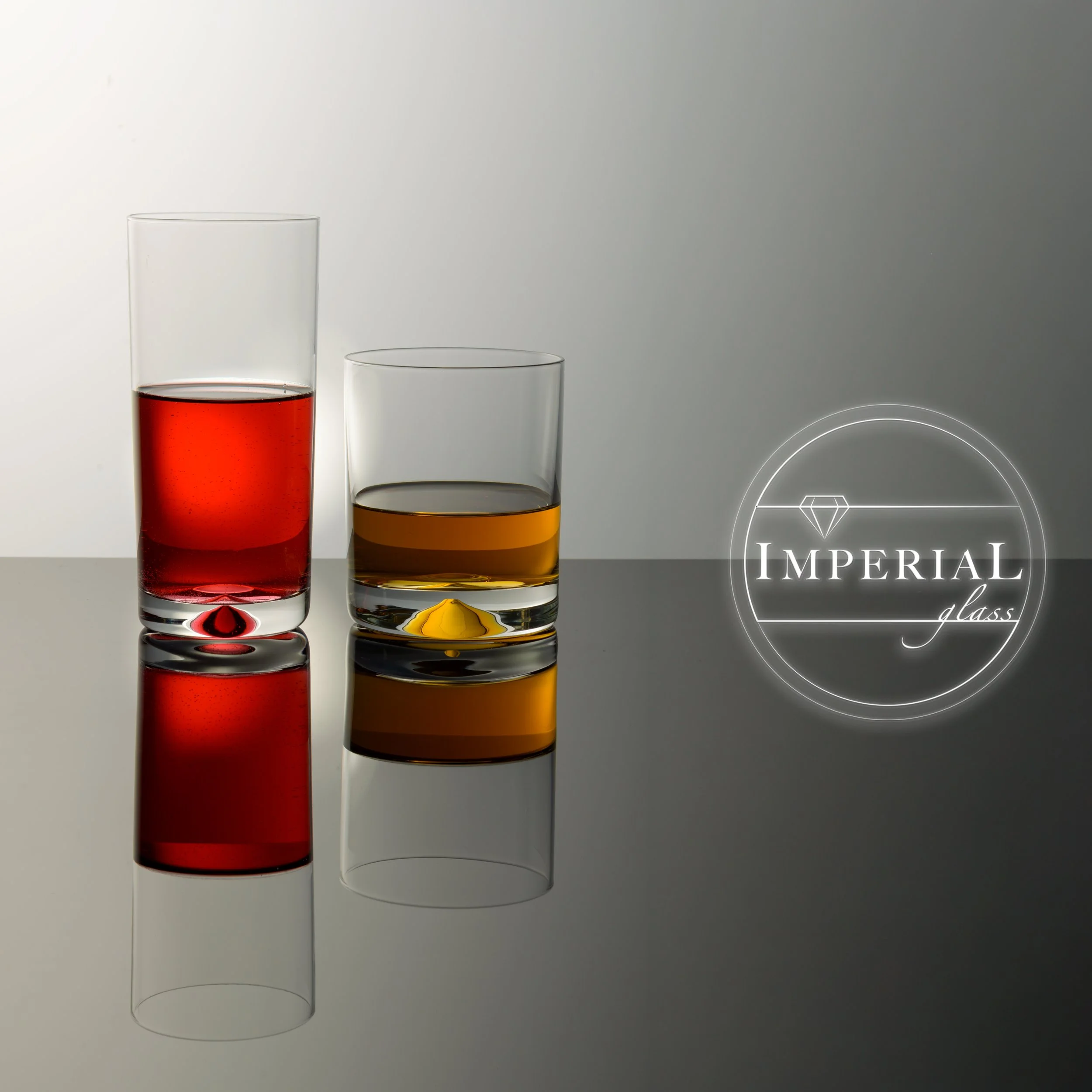 Zwei transparente Gläser, eines mit rotem Getränk, eines mit gelbem Getränk, auf einer weißen Oberfläche vor einem blassen grauen Hintergrund, mit einem weißen Kreis und einem Diamanten-Logo mit dem Text "Imperial glass" im unteren rechten Bereich.