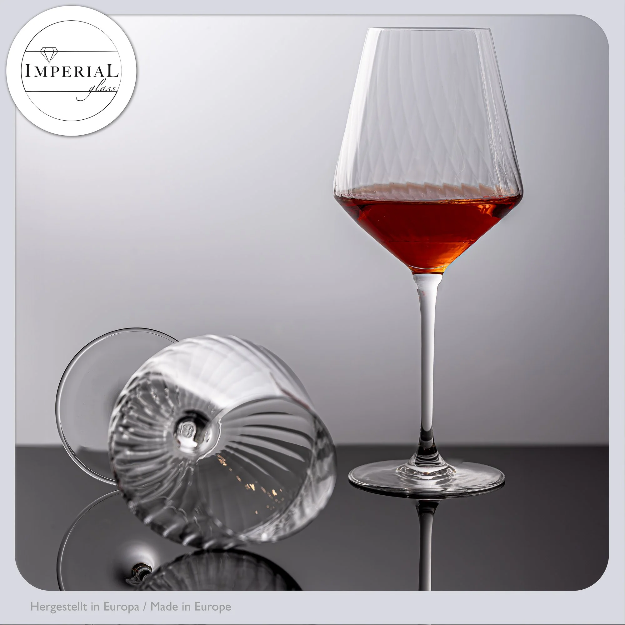 Ein elegantes Weinglas mit rotem Wein, umgeben von mehreren leeren Weingläsern, auf einem dunklen reflektierenden Tisch. Das Bild hat eine minimalistische und stilvolle Ästhetik.