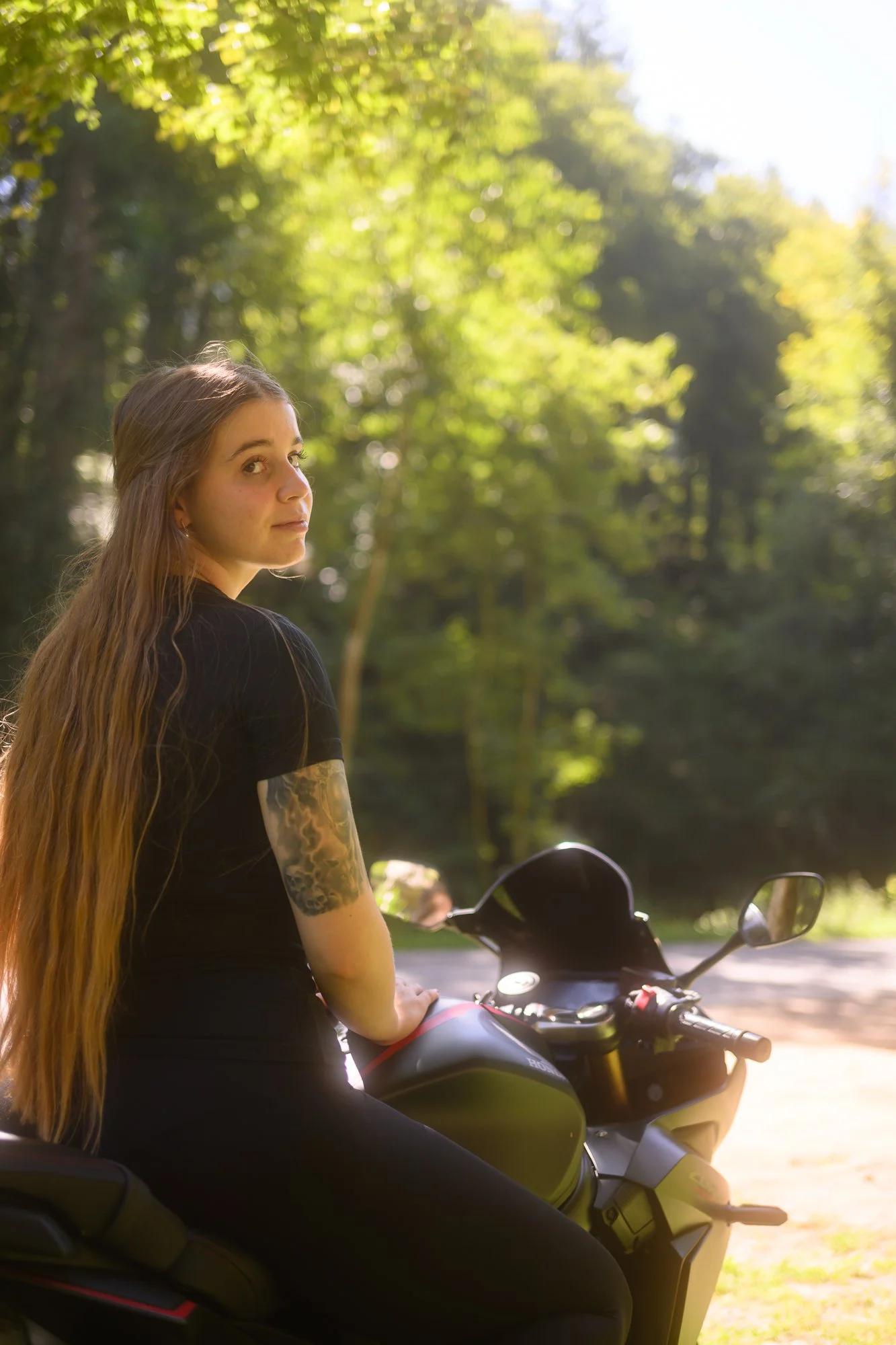 Junge Frau mit langen Haaren auf einem Motorrad im Park bei sonnigem Wetter.