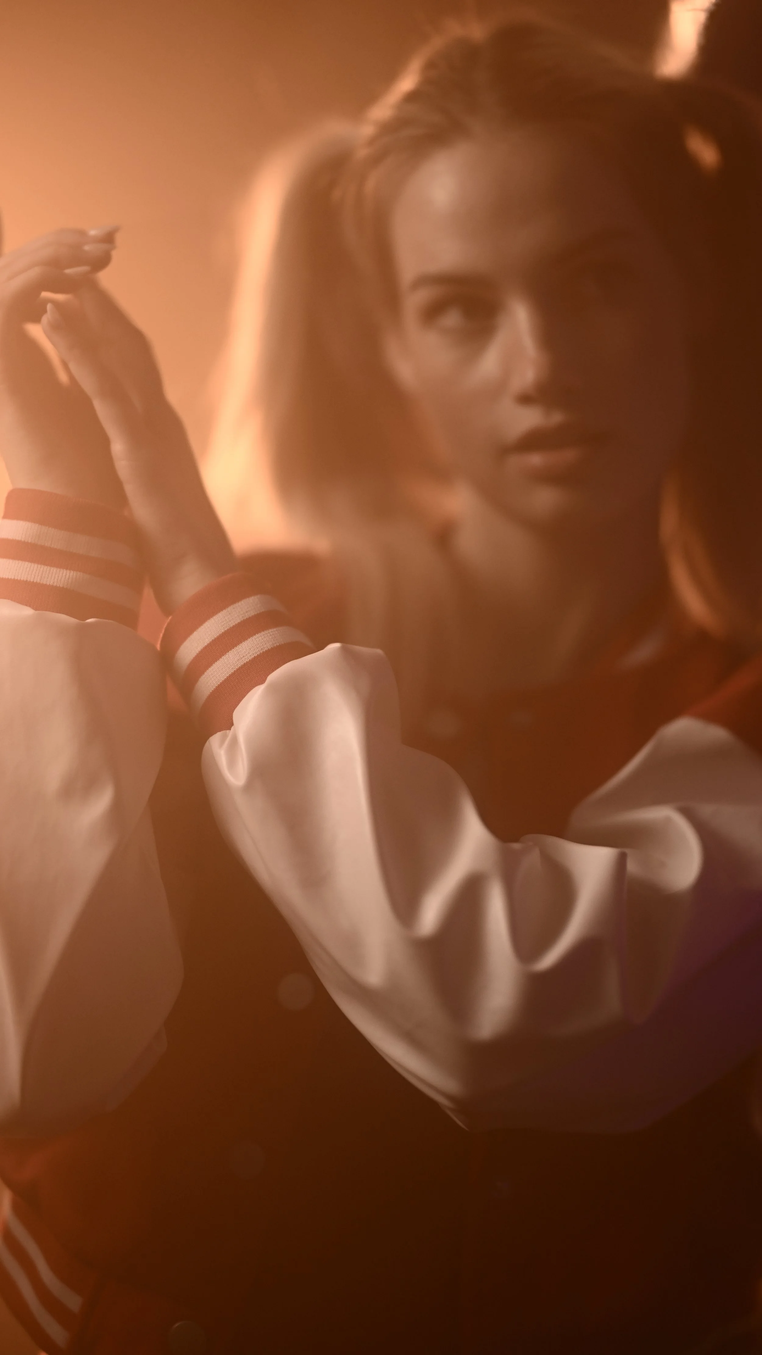 Nahaufnahme eines Models mit voluminösem, blondem Haar, die eine Jacke mit gestreiften Ärmeln trägt, vor einem warmen, unscharfen Hintergrund.