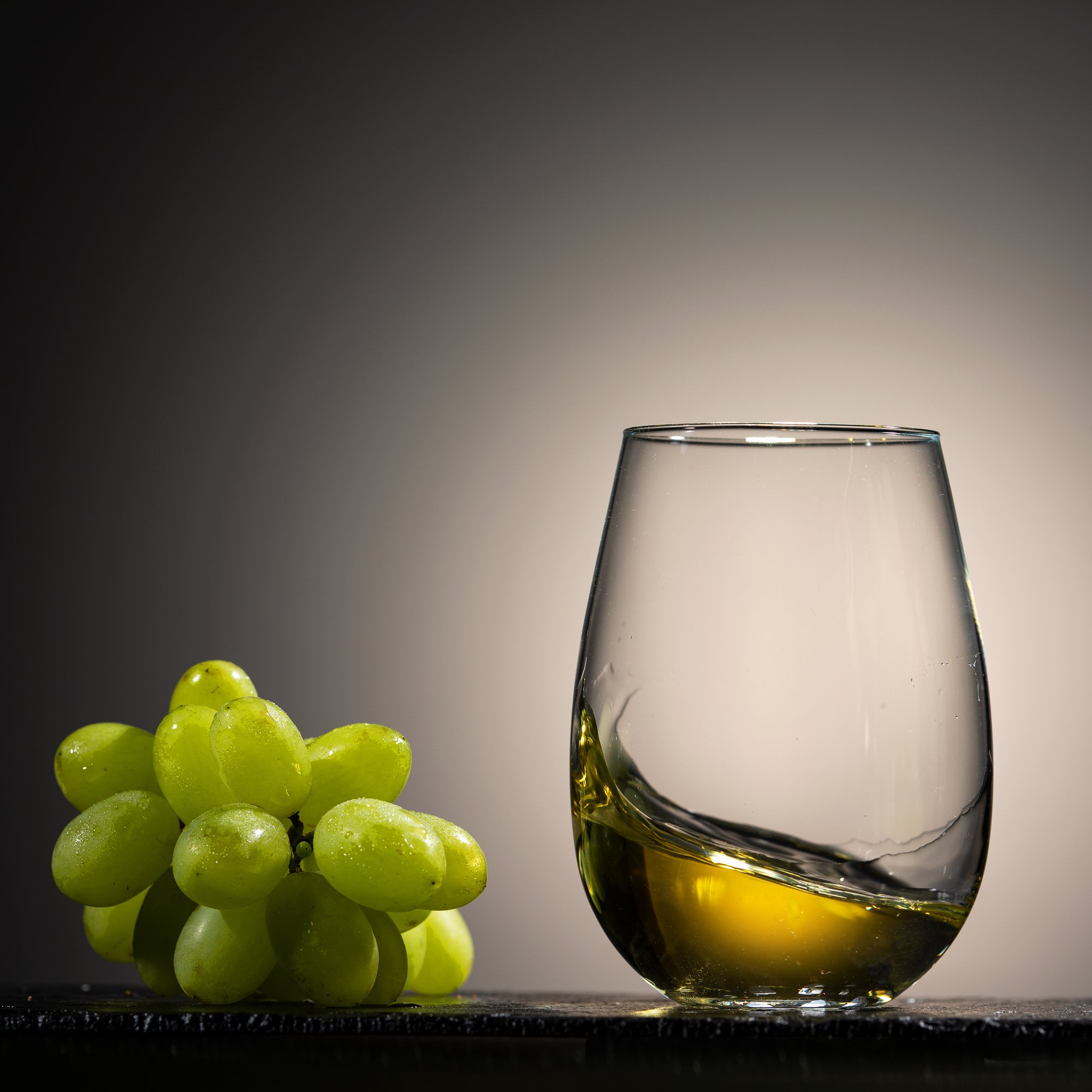 Grüner Weintraube, schwarzes Weinglas mit weißem Wein, dunkler Hintergrund, reflektierende Oberfläche