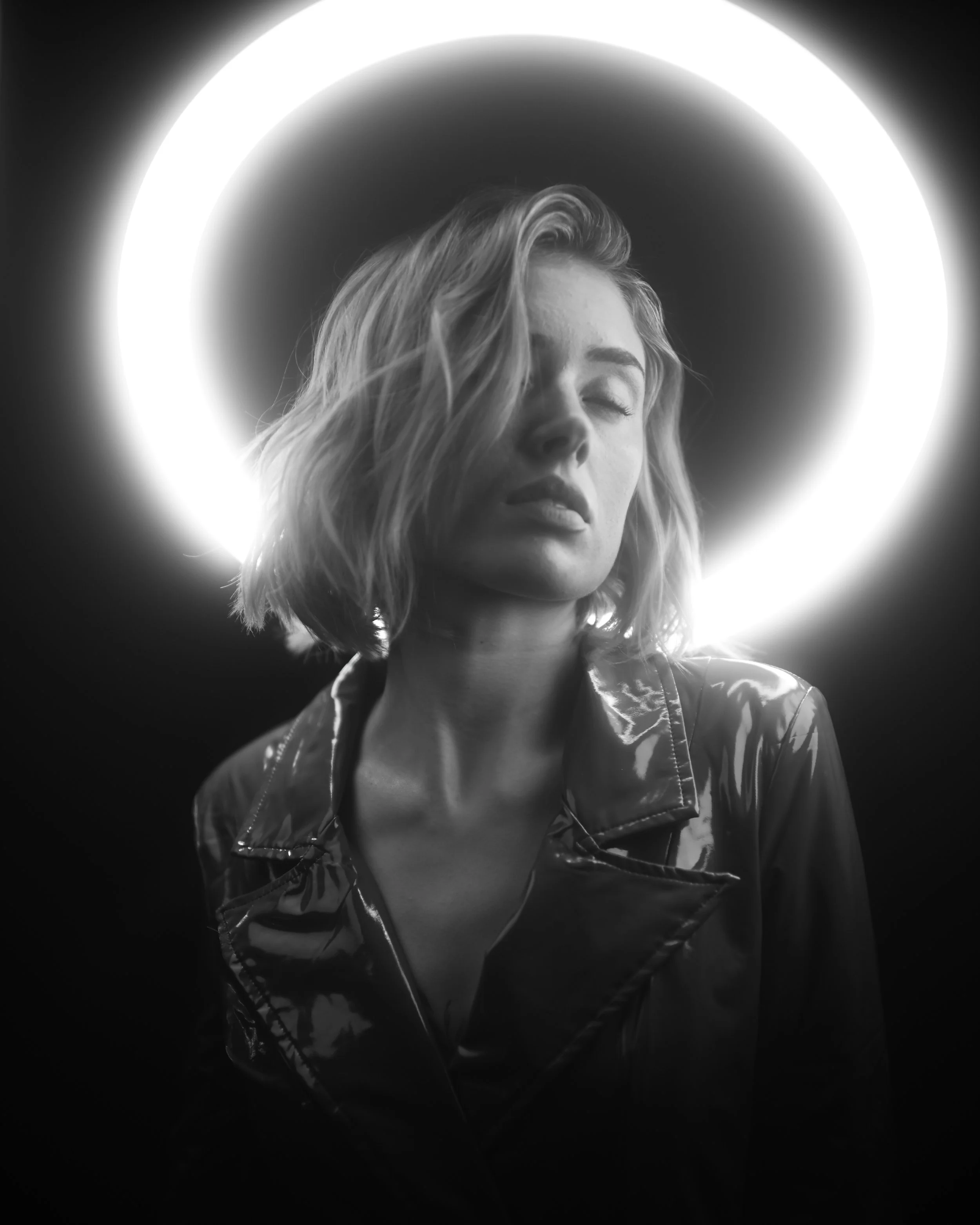 Schwarz-weiß-Foto eines entspannten Mädchens mit geschlossenen Augen, umgeben von einem leuchtenden Ring, im Lichtkreis, getragen von einer Jacke.