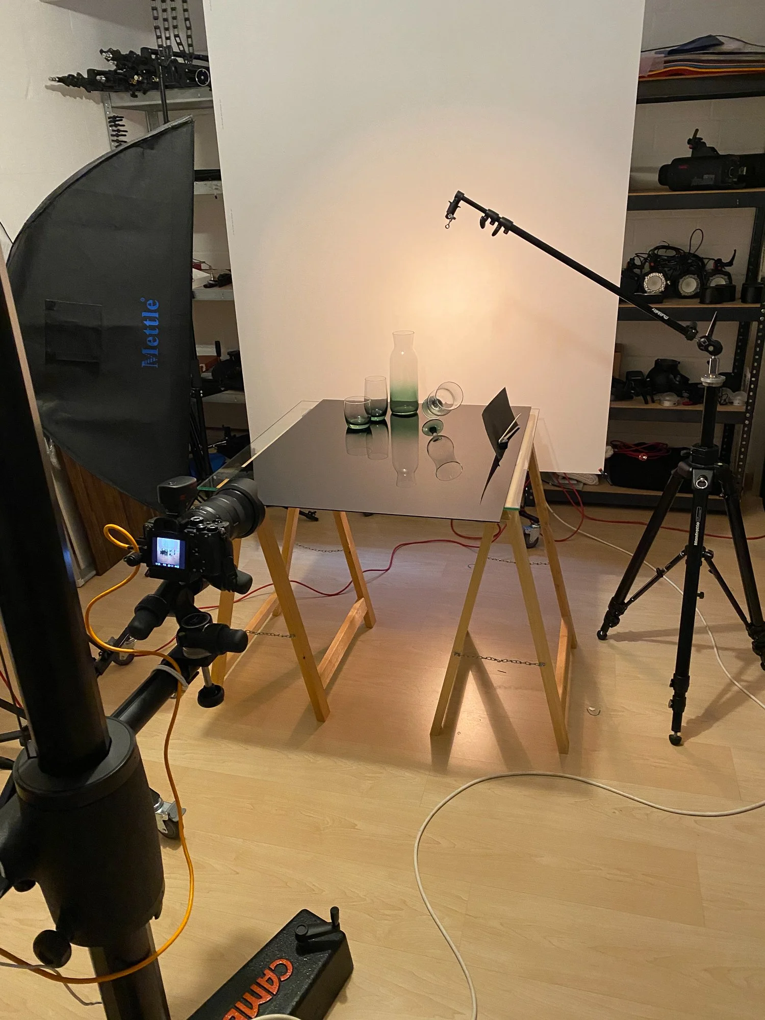 Fotostudio mit Kamera, Lichtquellen und Reflektor, in dem eine Vase mit mehreren Gläsern und einer Kapsel steht.
