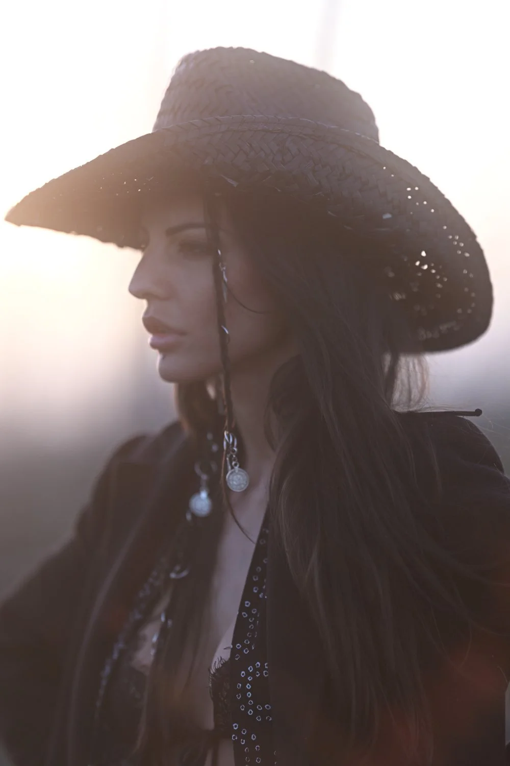 Eine Frau trägt einen breite Strohhut und schaut nach links bei Sonnenuntergang.