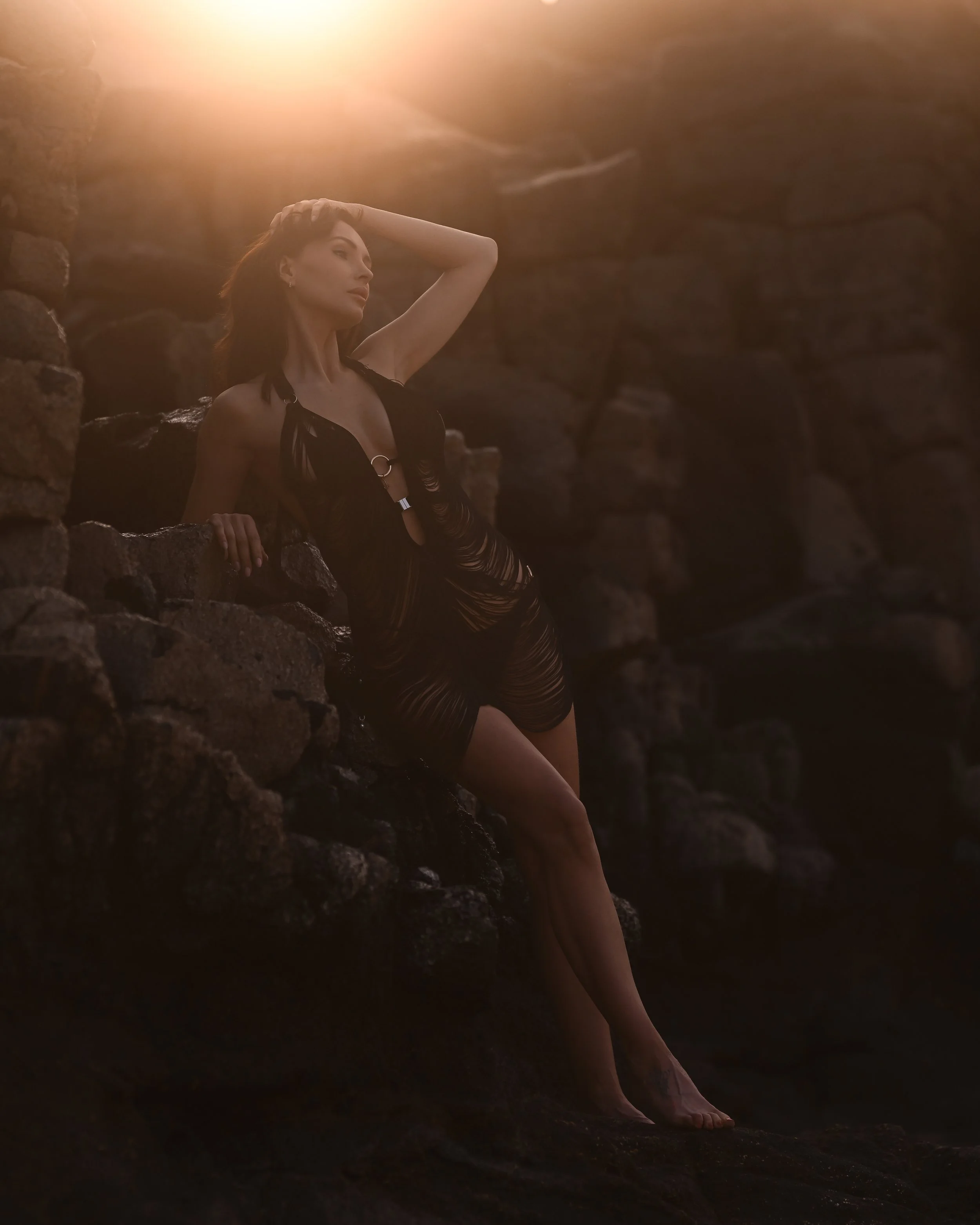 Frau mit schwarzen Kleid auf felsiger Küste bei Sonnenuntergang