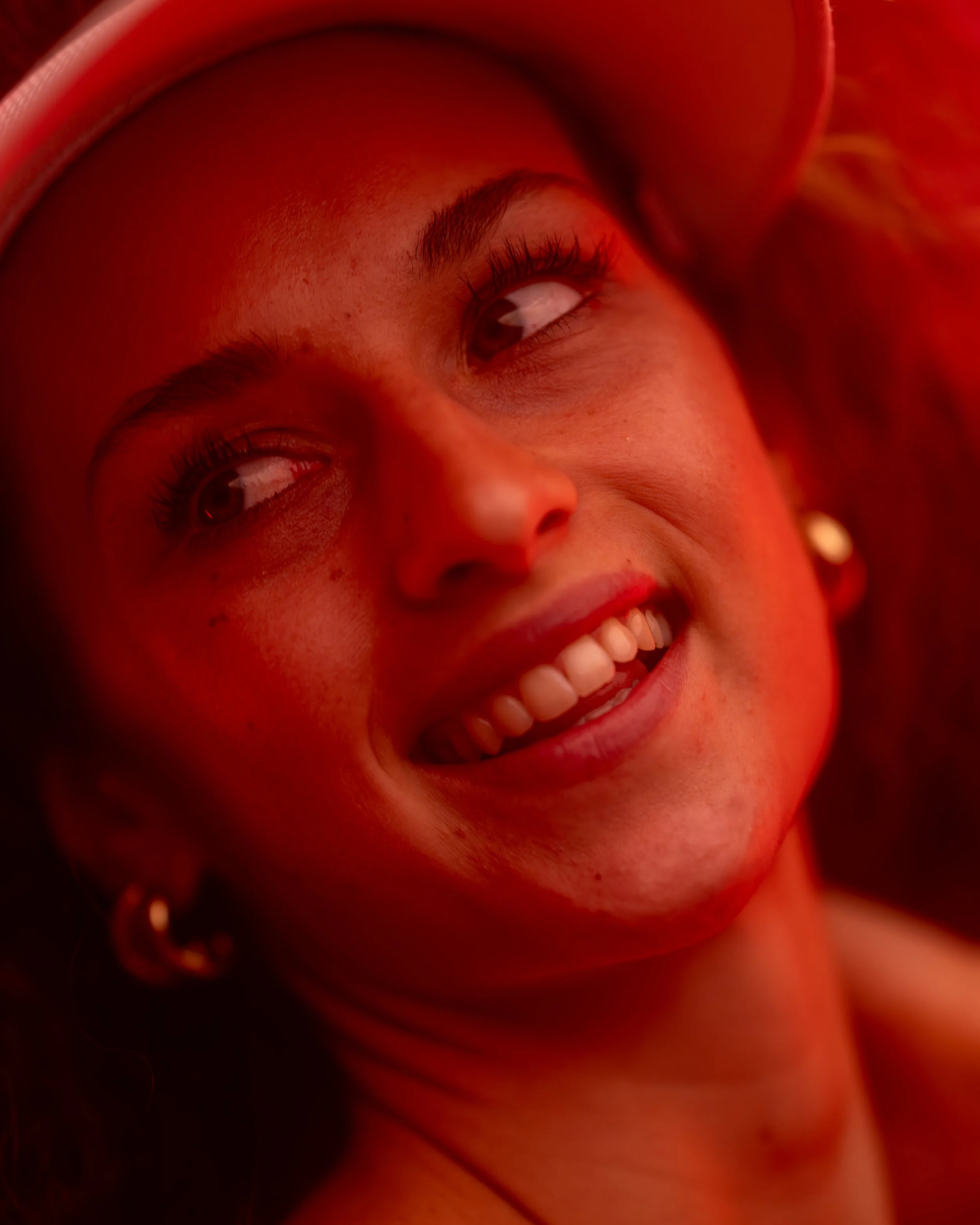 Nahaufnahme eines lachenden Mädchens mit gelocktem Haar und einem Hut, das in gelbem Licht leuchtet.