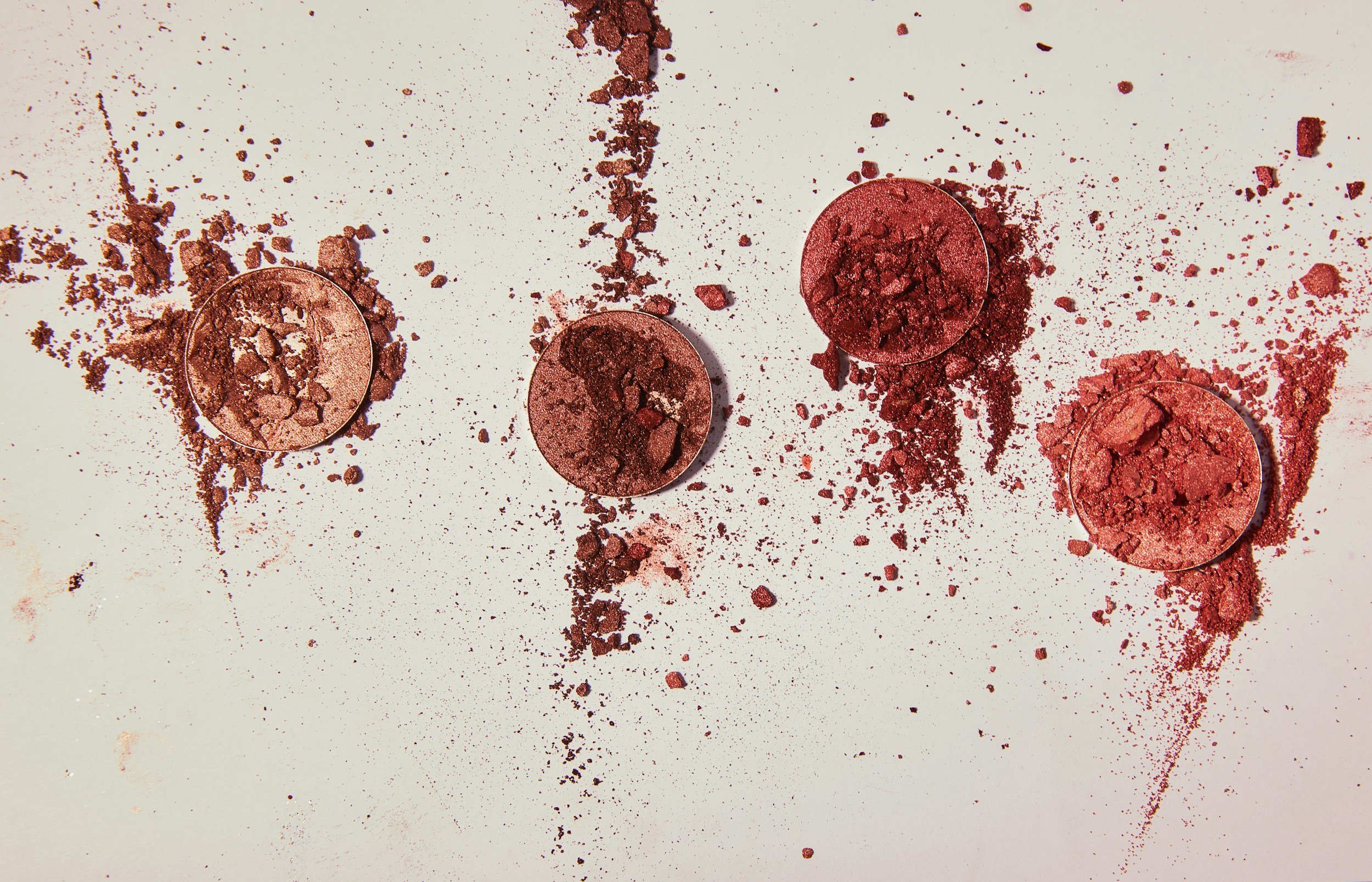 Various shades of pink and red crushed eyeshadow eyeshadow scattered across a white surface.