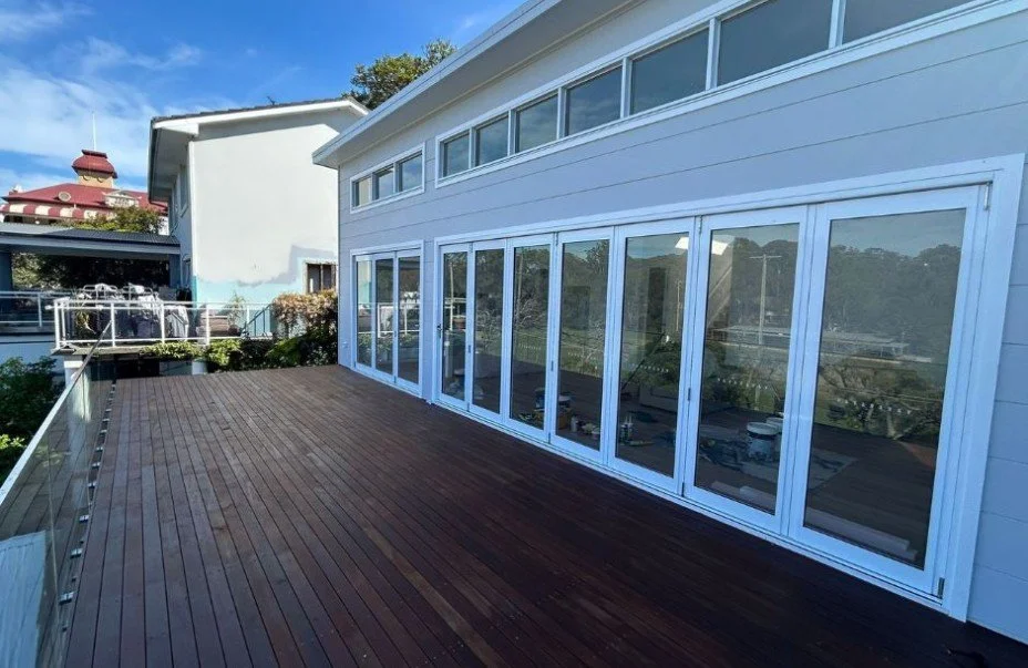 A spacious outdoor wooden deck attached to a modern house with large glass sliding doors and windows.