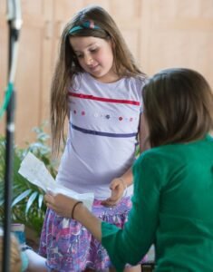 A young girl and an adult woman looking at a piece of paper together inside a home.