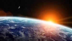 View of Earth from space with the Sun on the horizon and a visible moon in the sky.