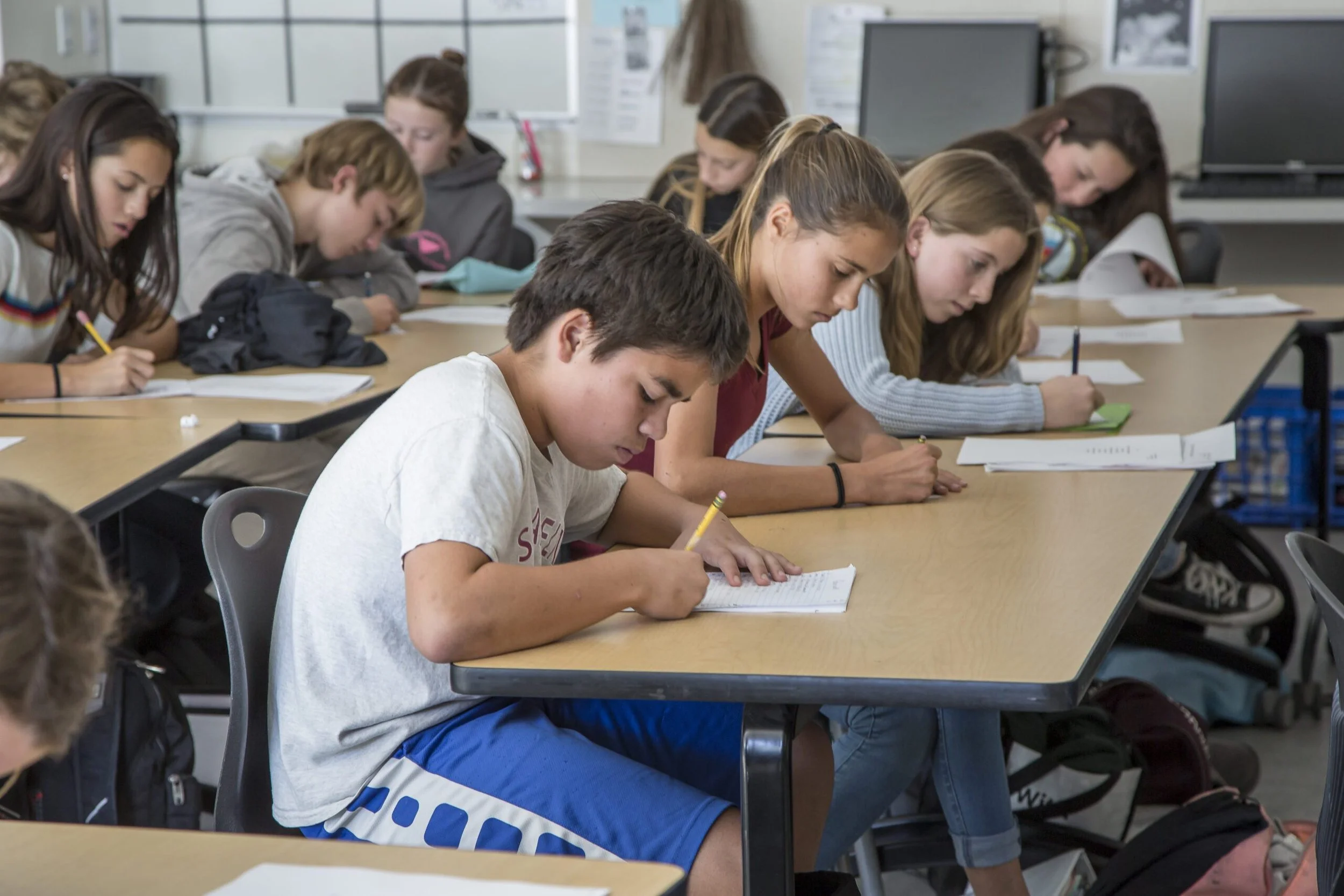Students sitting at desks in a classroom, all focused on writing on papers in front of them.