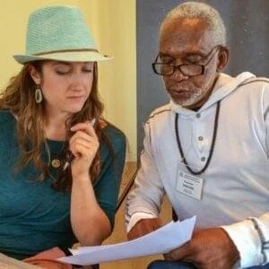 A young woman and an older man looking at papers together at a table, in a professional setting.
