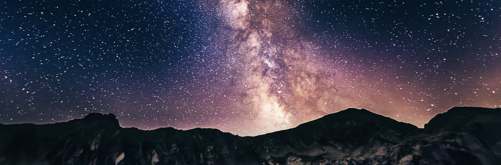 Night sky filled with stars and the Milky Way galaxy above a mountain silhouette.