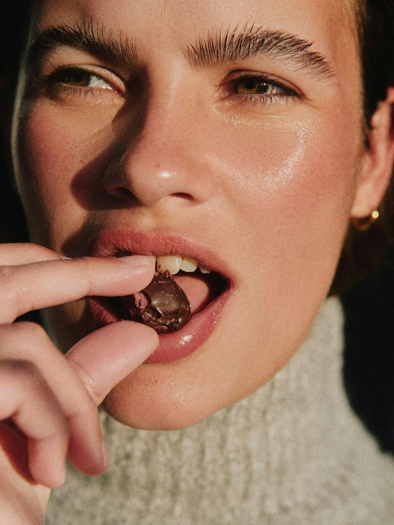 Close-up of a woman with fair skin licking a chocolate cookie with pink filling.
