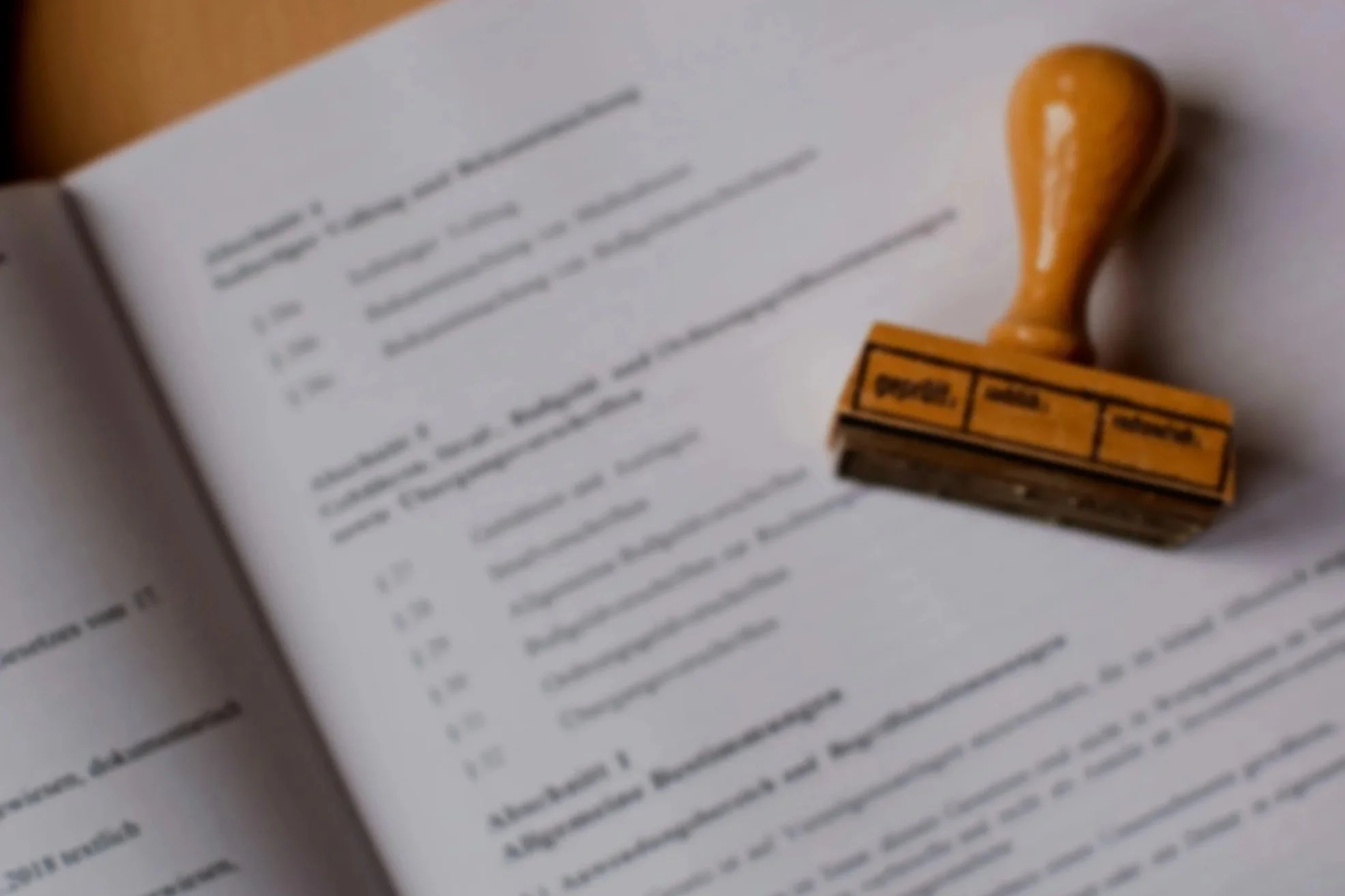 Eine offene Buchseite mit blauer Tinte geschriebenem Text, rechts daneben ein Holzstempel mit orangefarbenem Griff und schwarzem Text auf der Stempelfläche.