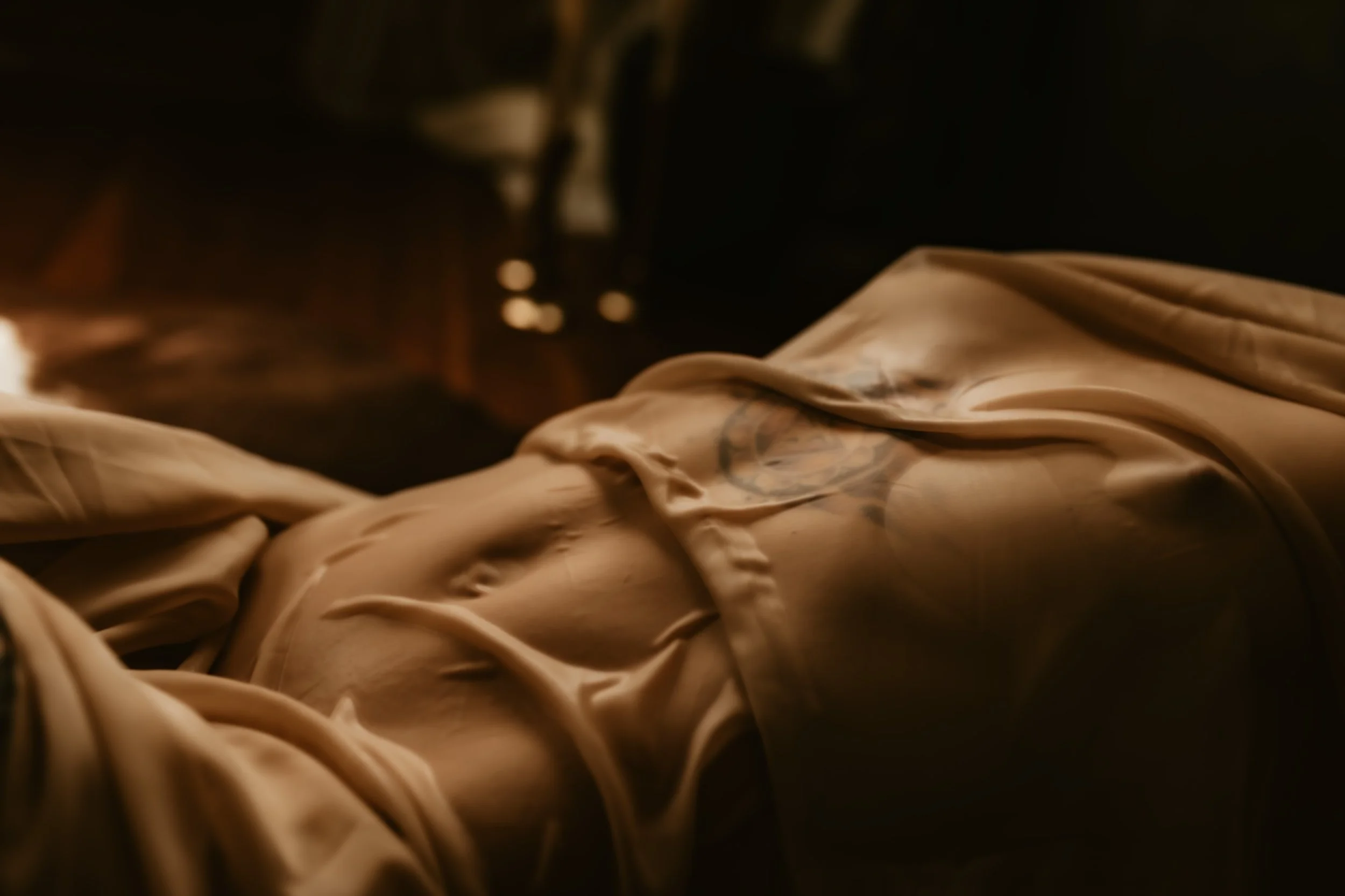 Close-up of beige crumpled fabric with a tattooed arm partially visible.