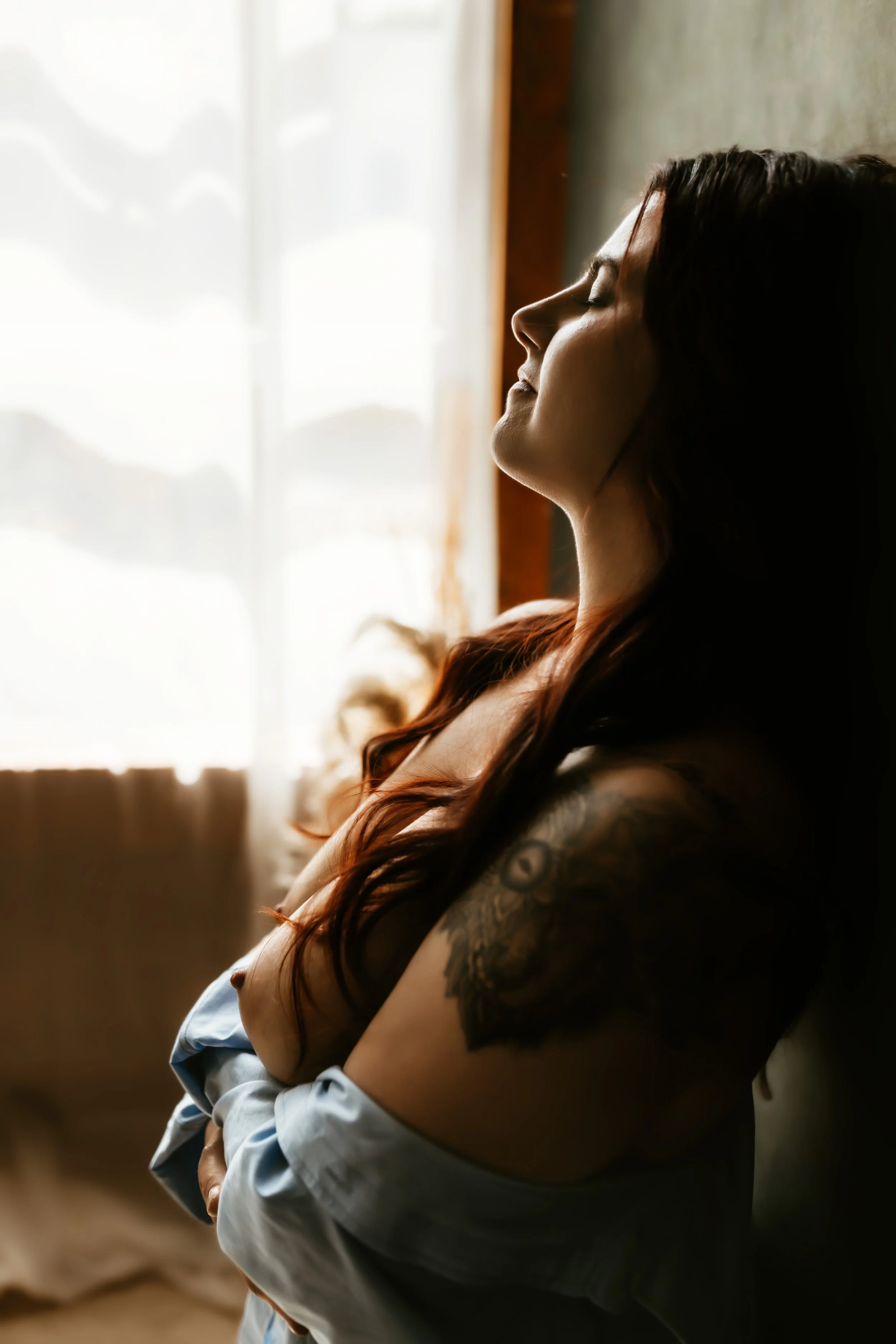 A woman with closed eyes standing near a window with sunlight shining through.