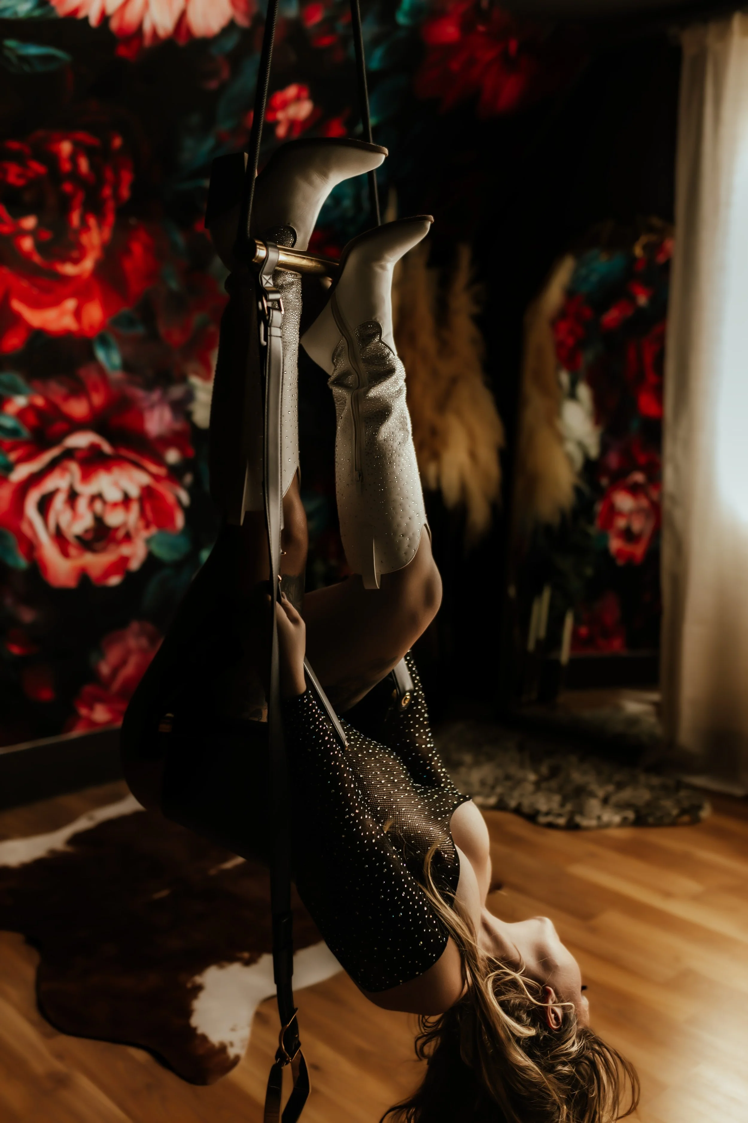 A girl dressed in a sparkly black dress and heels, laying on the floor with her head turned upside down, holding a black handbag, in front of a floral wallpaper background.