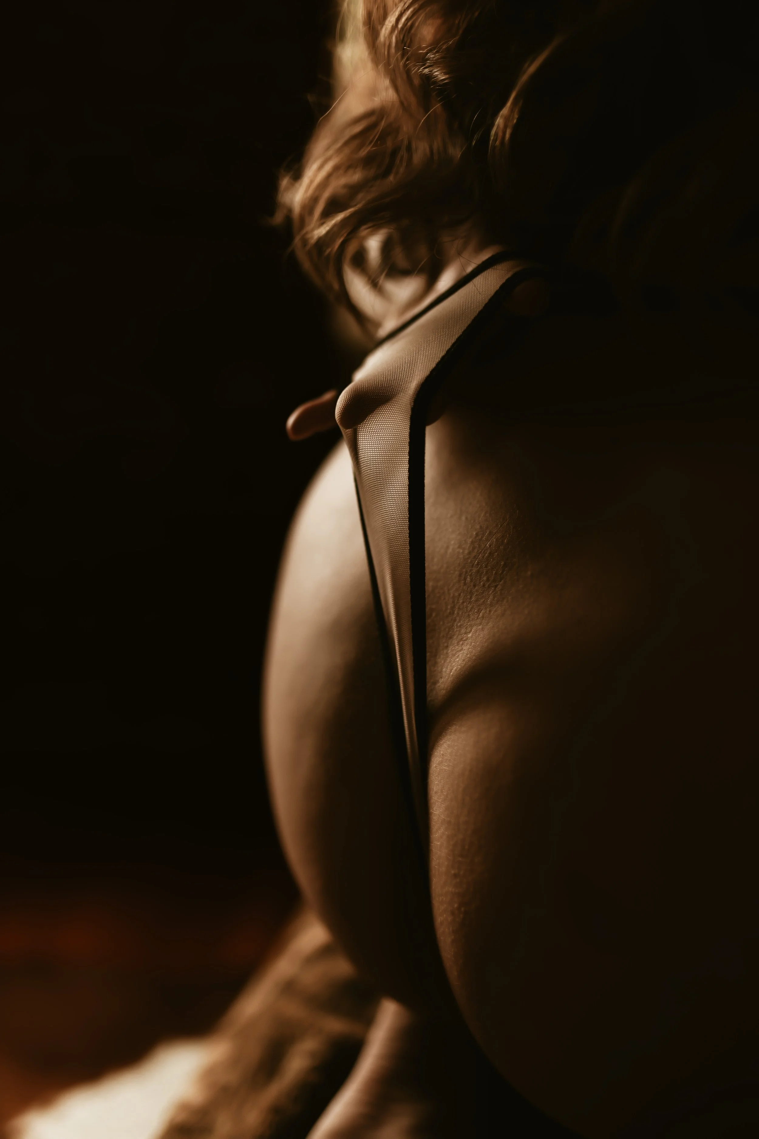 Close-up of a woman's back with fishnet garment and smooth skin, illuminated by soft light, against dark background.